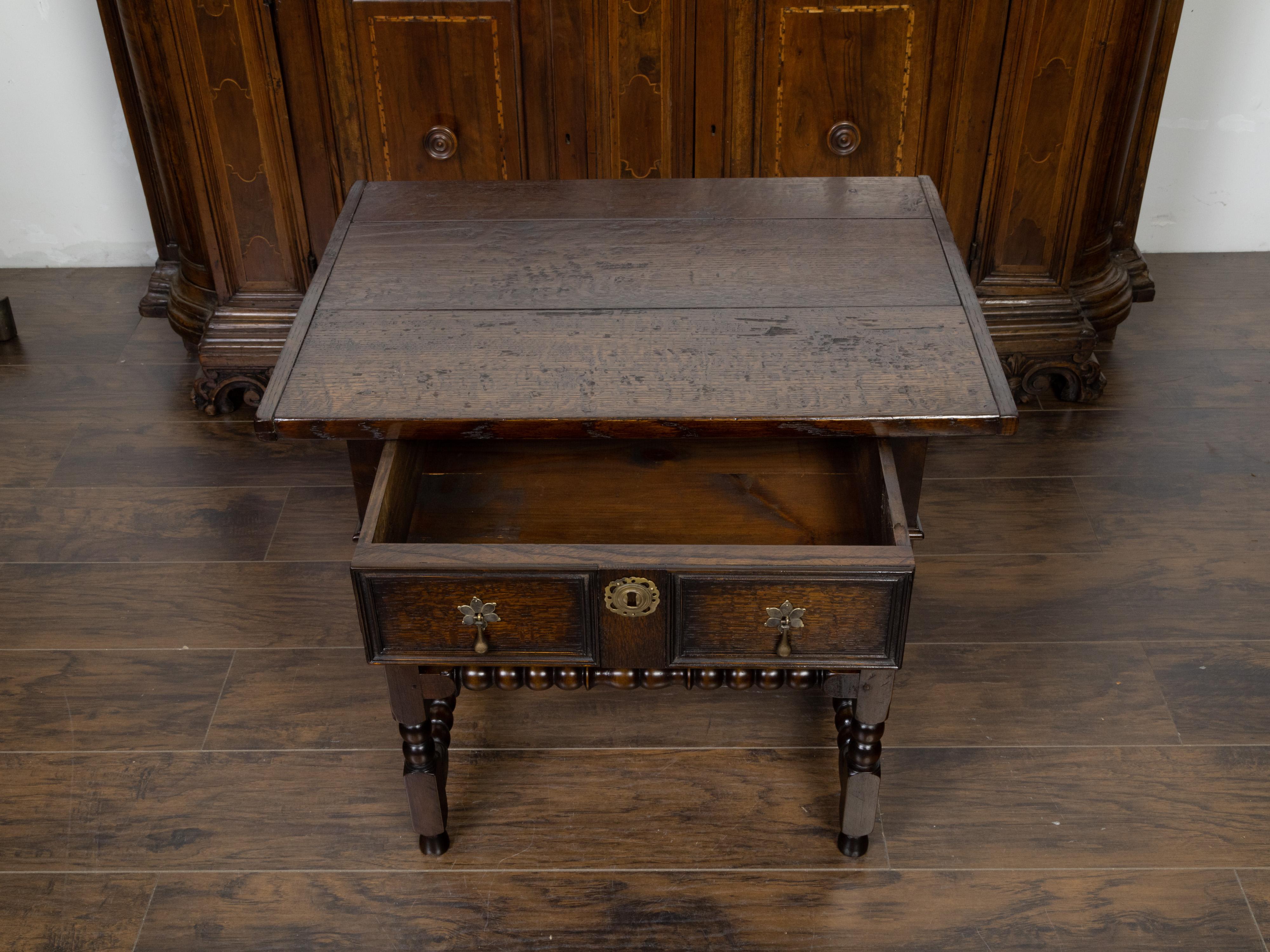 An English oak side table from the 19th century, with single drawer and bobbin accents. Created in England during the 19th century, this oak side table features a rectangular planked top sitting above a single drawer with molded panels and brass