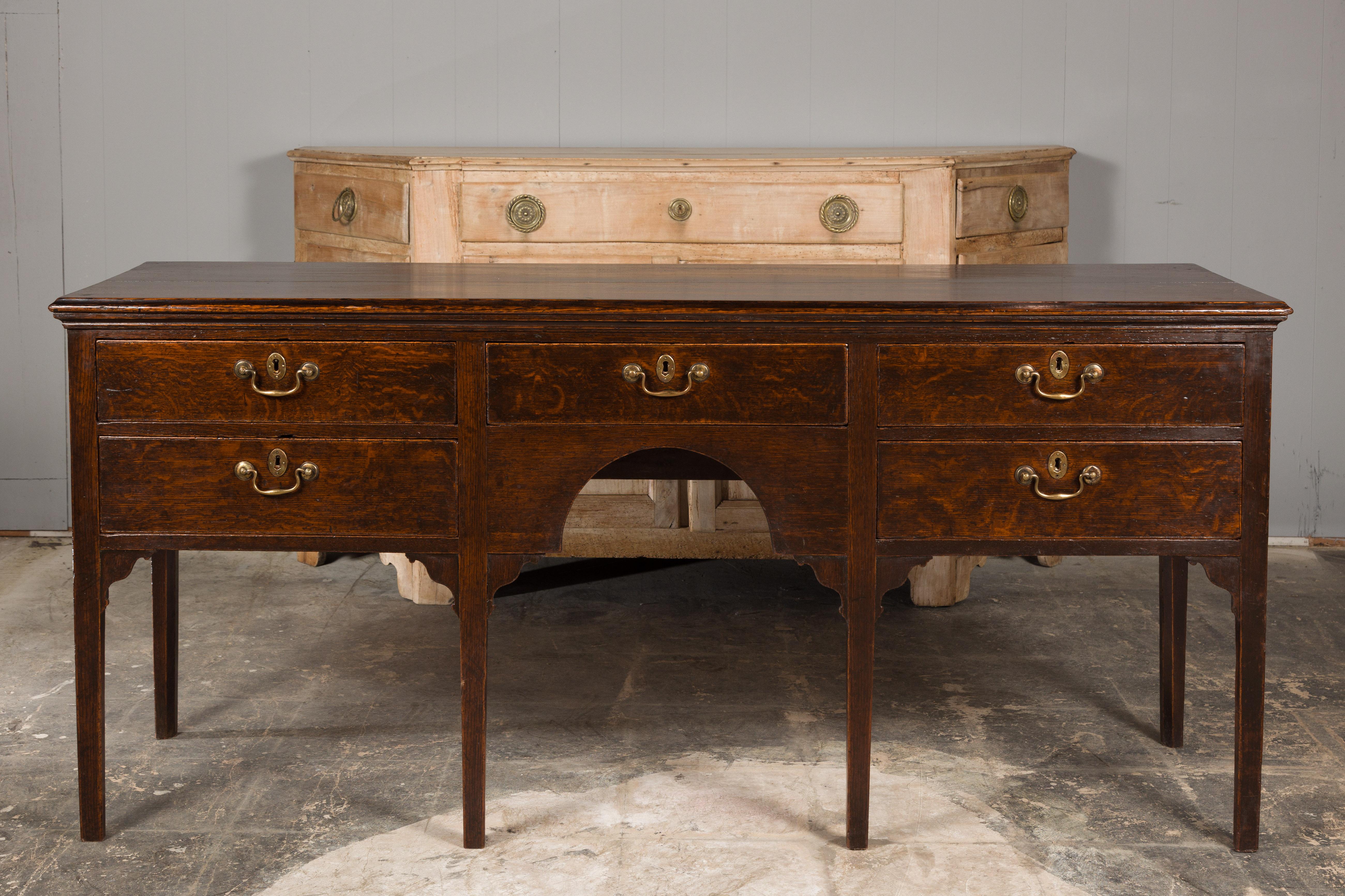 An English oak sideboard from the 19th century with five drawers, brass hardware, carved spandrels and straight legs. Imbue your interior with an air of timeless sophistication with this exquisite English oak sideboard hailing from the 19th century.