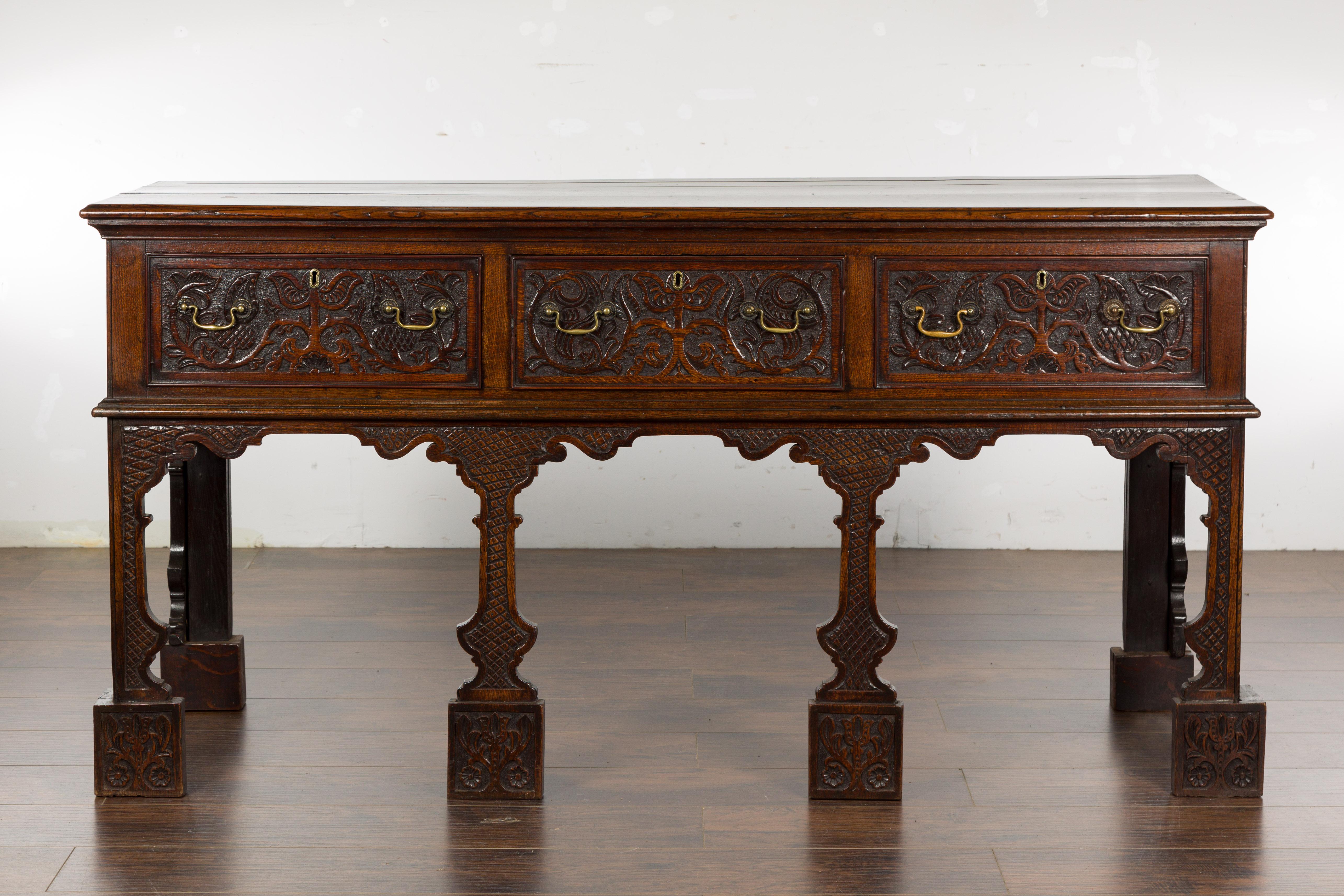 An English oak sideboard from the 19th century with three low-relief carved drawers, carved legs and brass hardware. Immerse yourself in the charm and splendor of the 19th century with this elegant English oak sideboard. This piece is crafted with