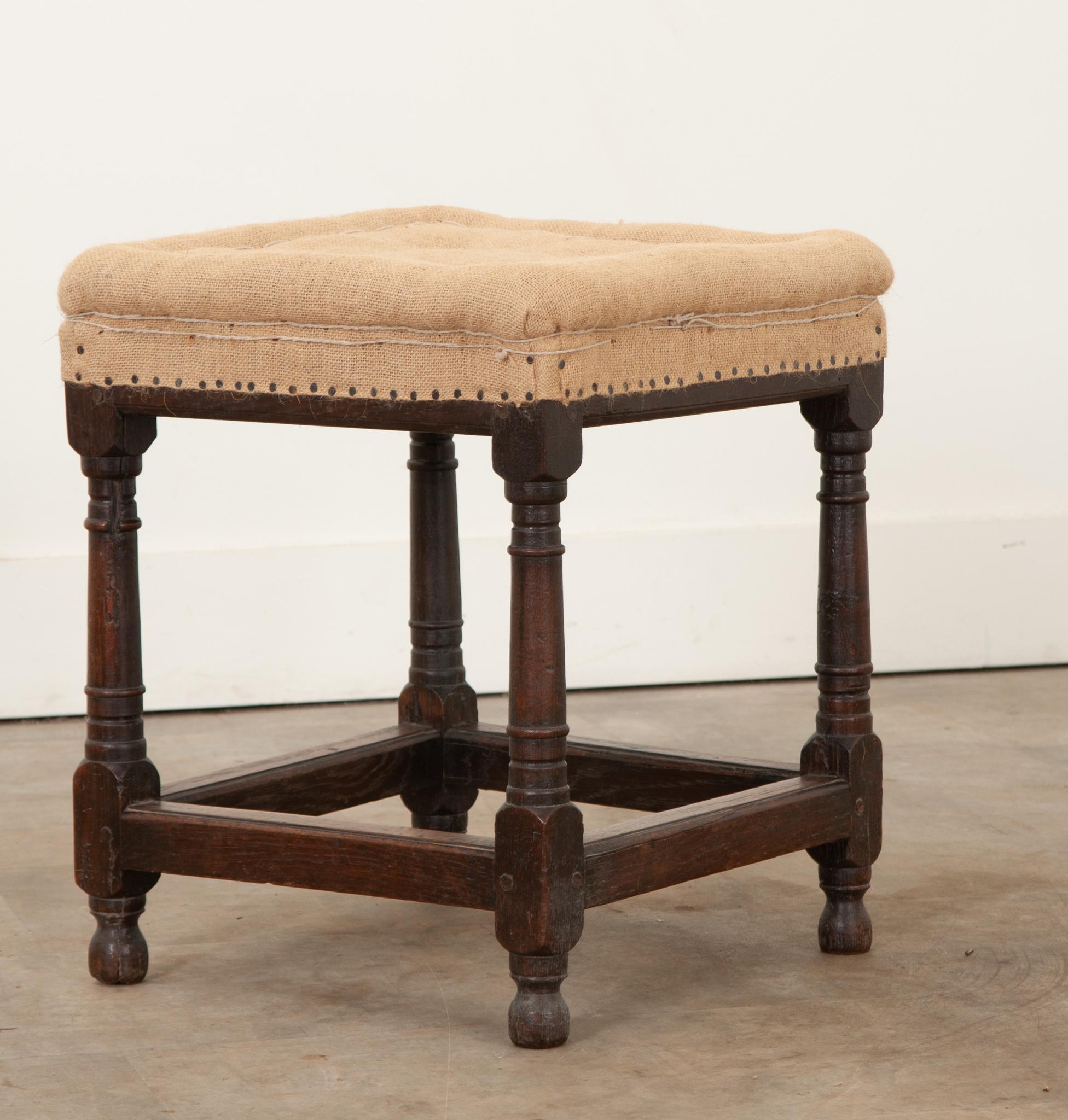 A sturdy, hand carved, solid oak stool from the 1800’s. The top cushion is filled with horse hair and is ready for its next layer of upholstery. The firm cushion is resting over four turned and carved dark oak legs connected with stretchers, adding