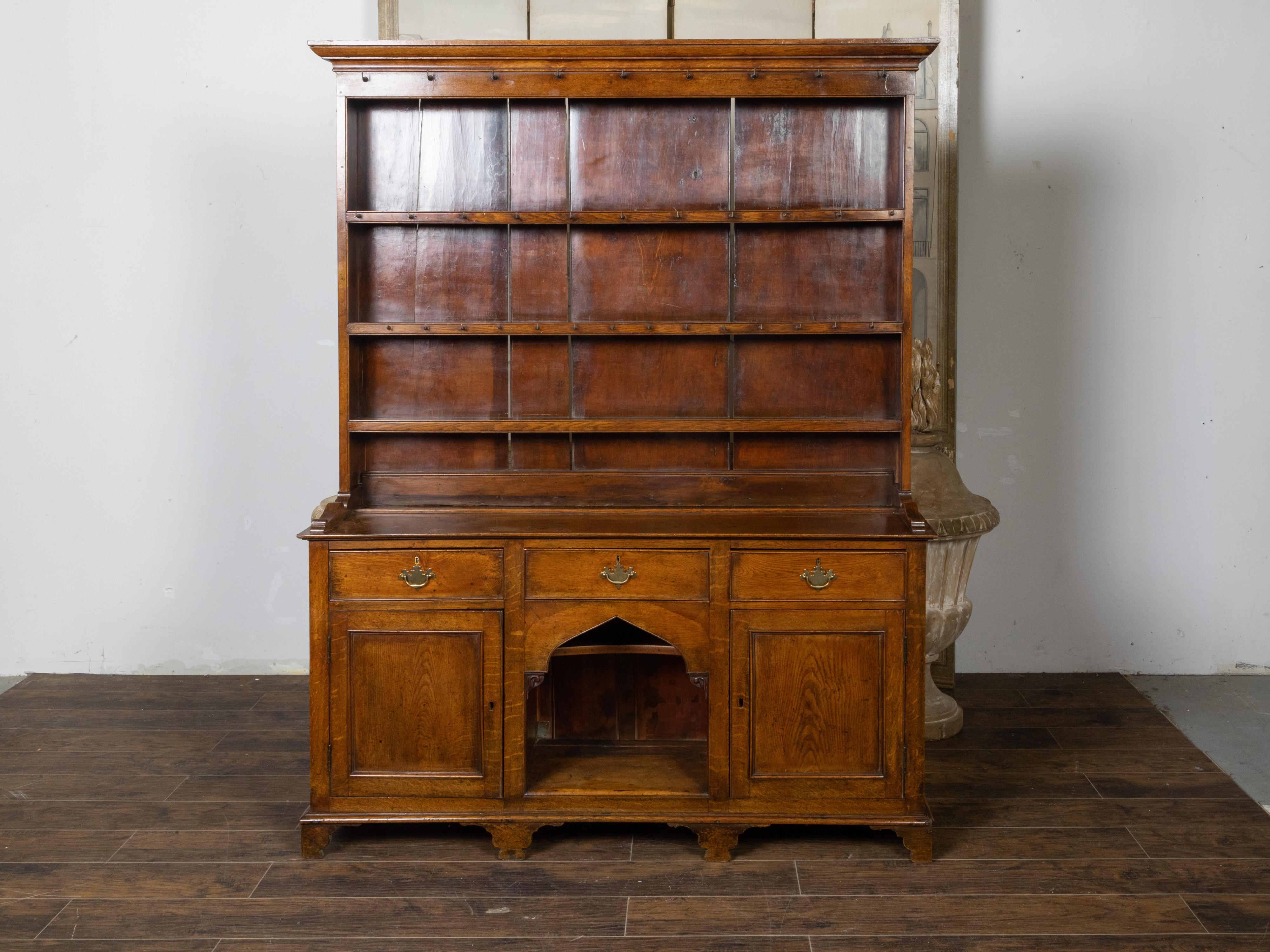 An English oak Welsh dresser from the 19th century, with open shelves, petite hooks and low sideboard with two doors, three drawers, carved arch and Chippendale style hardware. Created in England during the 19th century, this oak Welsh dresser