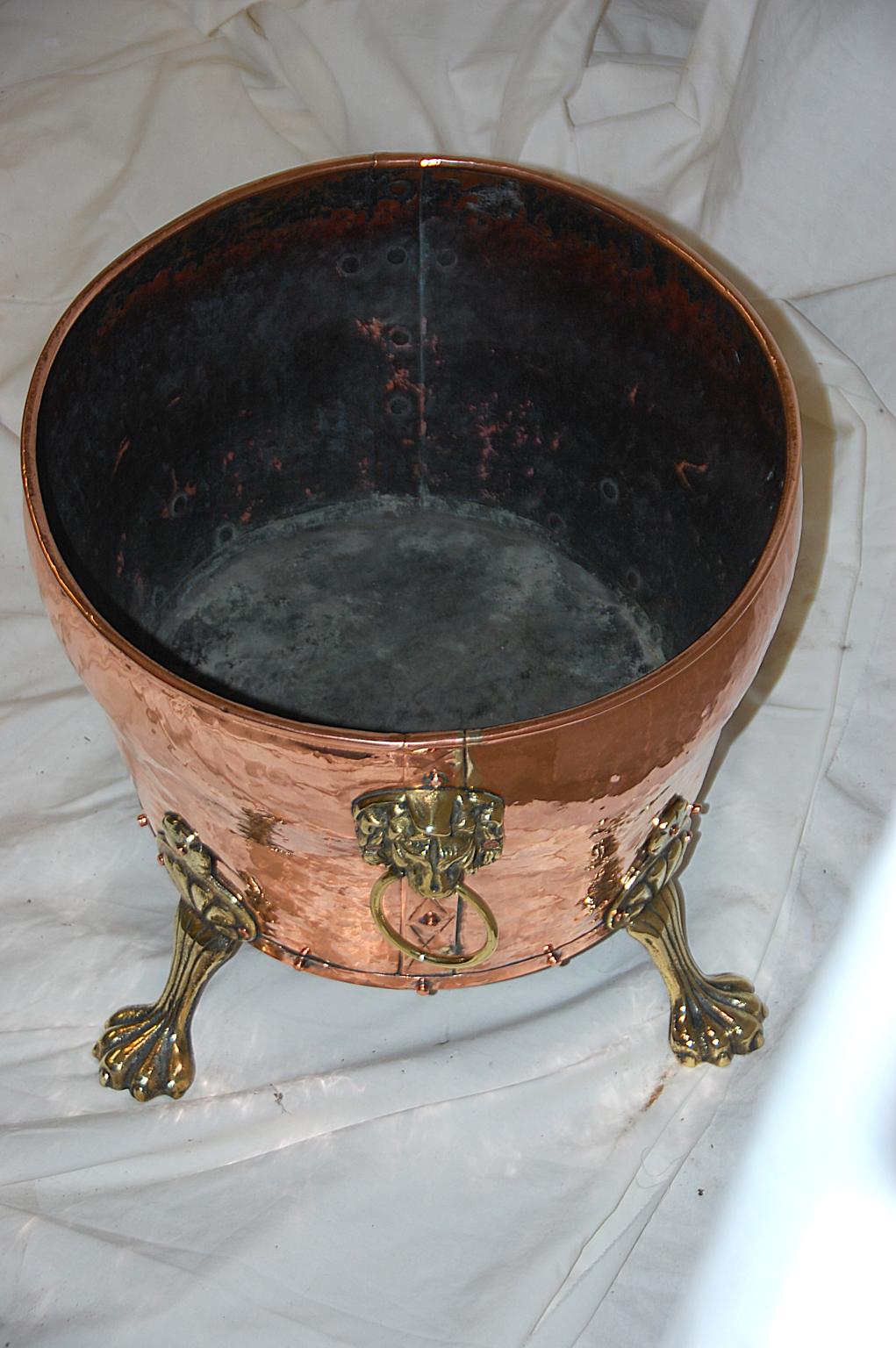 English mid 19th century oval copper coal bin with cast brass paw feet and lion headed side handles. This shaped oval coal bin is made with riveted construction techniques, is of quite heavy quality and would make among other things a good log bin,