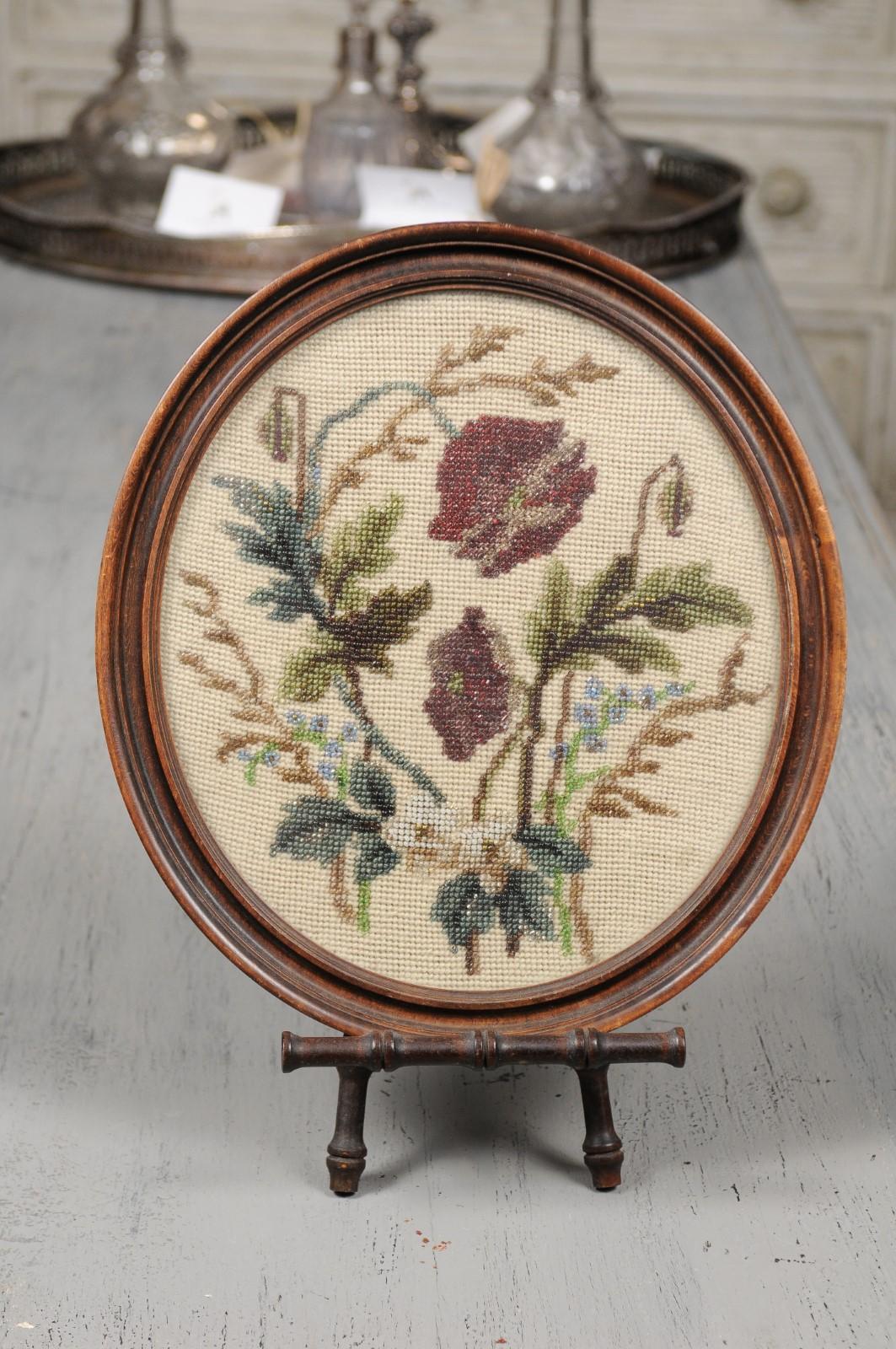 An English Victorian floral needlepoint and beading tapestry from the 19th century set in an oval frame and raised on a stand. Born in England during the reign of Queen Victoria, this charming decorative object features an oval wooden frame