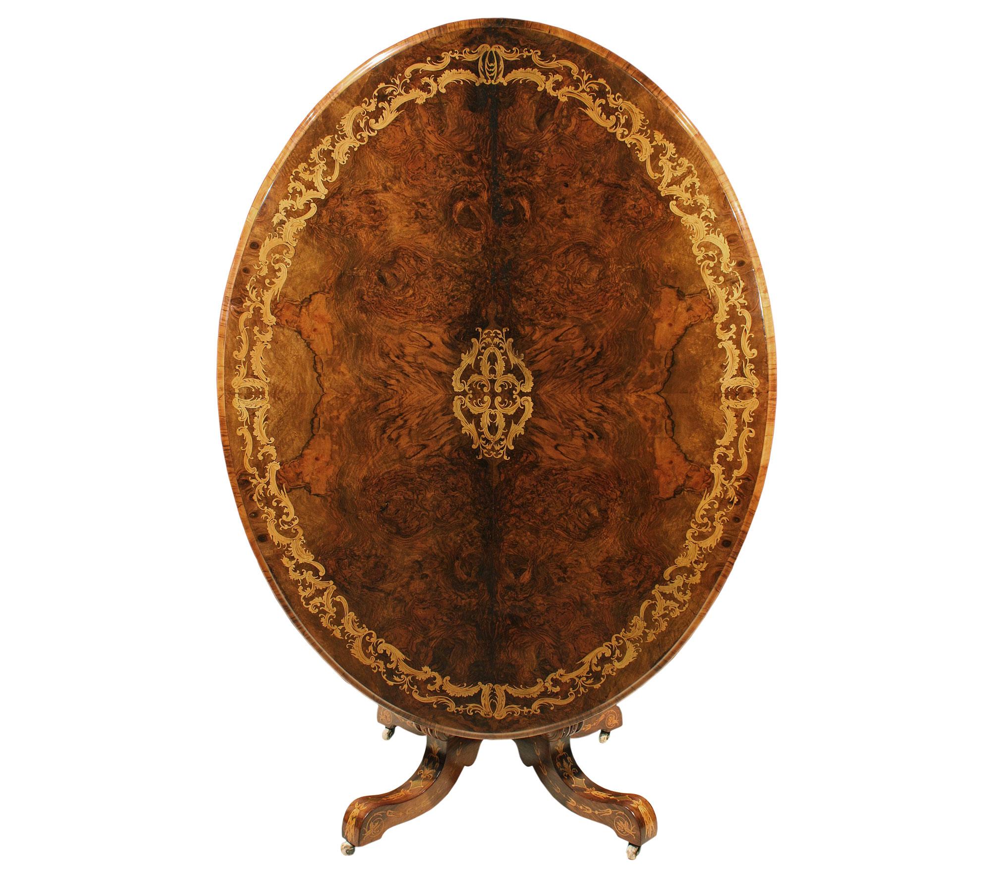 A very decorative and large scale English 19th century oval tilt top center table in various walnuts and exotic woods. The table is raised by the original porcelain casters with four C scrolled supports joined by a richly inlaid bottom tier. The