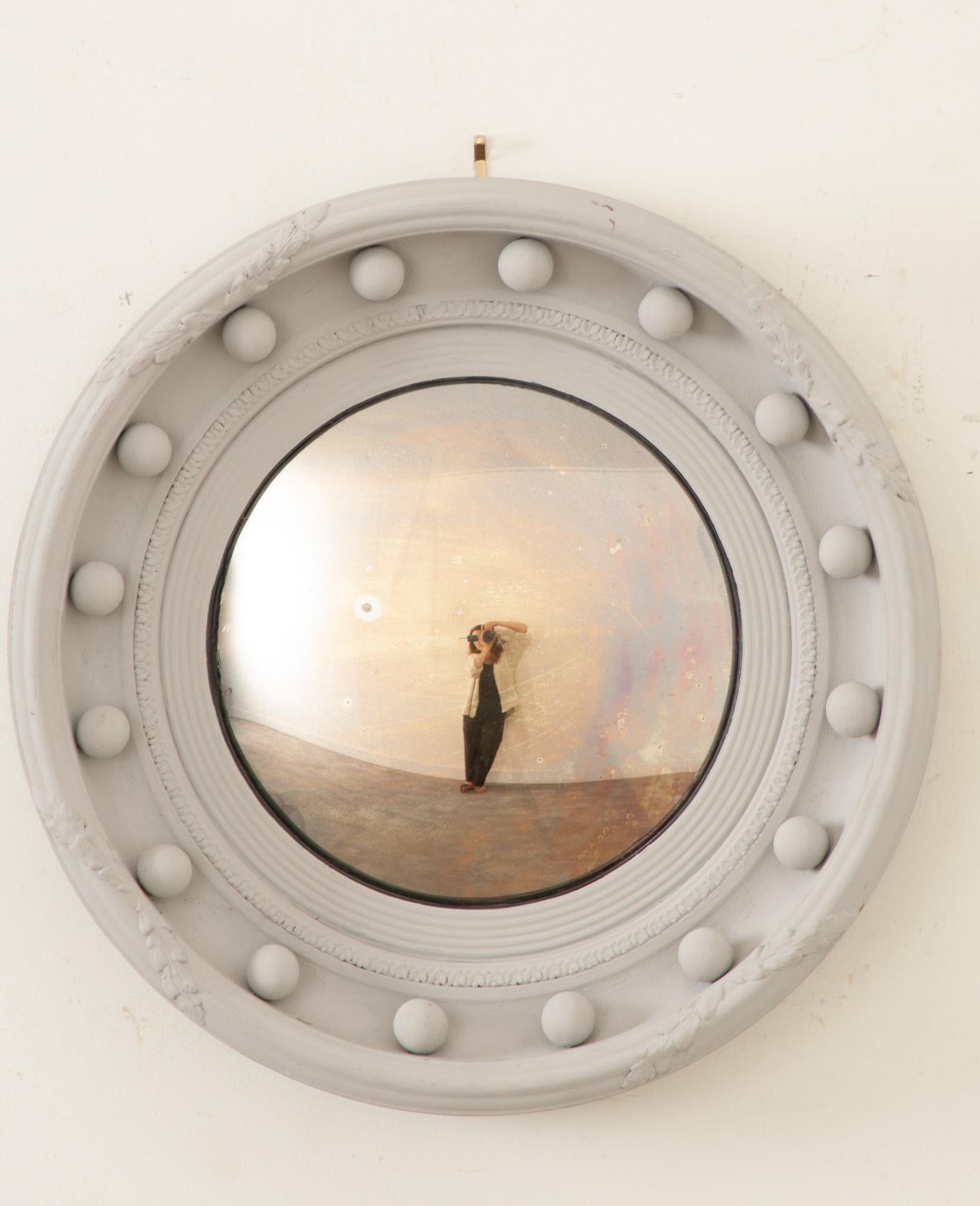 An English 19th century convex bullseye mirror with petite spheres and painted finish. This stylish circular mirror features the original convex mirror plate, with the gorgeous signs of age and foxing, reflecting and distorting images beautifully,