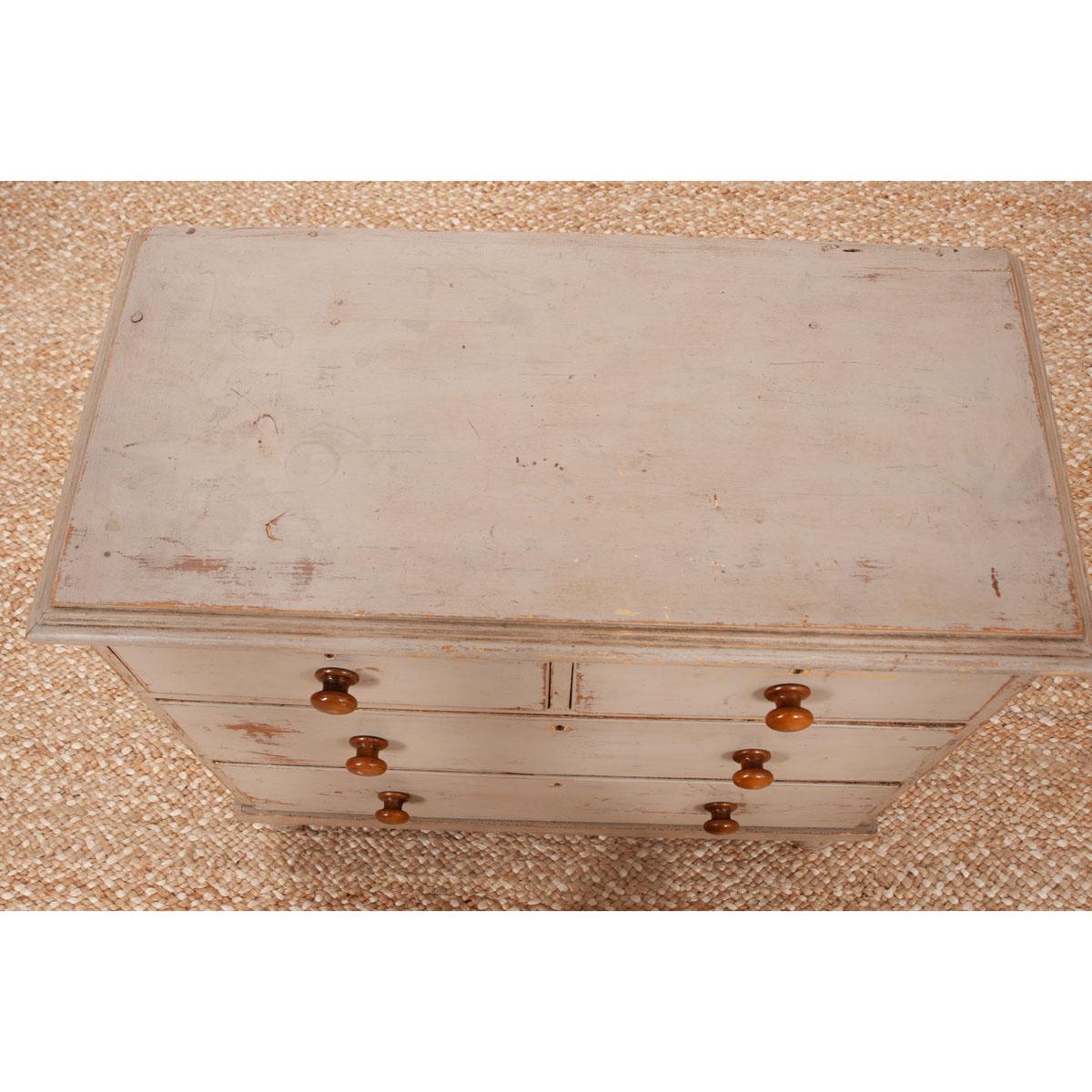 A small painted, four drawer chest from 19th century England. Layers of paint add depth and character to this piece. A gray-ish/green color is the top layer with yellow, white and bare wood showing through. The four drawers each have natural stained