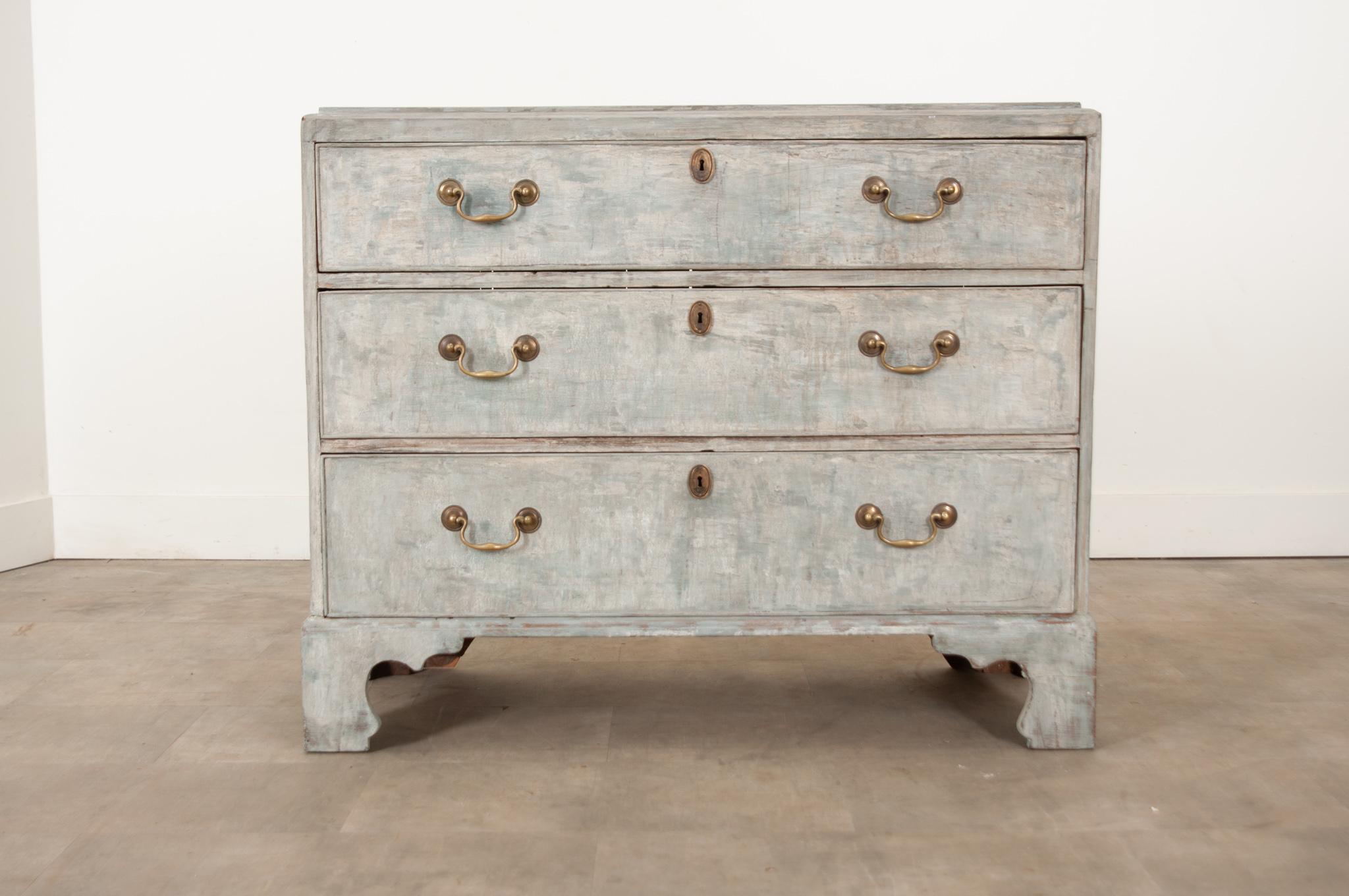 A streamlined profile and stylish bracket legs make this 19th century British stripped and painted commode a standout. This recently painted case piece has smooth plain  top with a deep molded edge above three large drawers with oval escutcheon