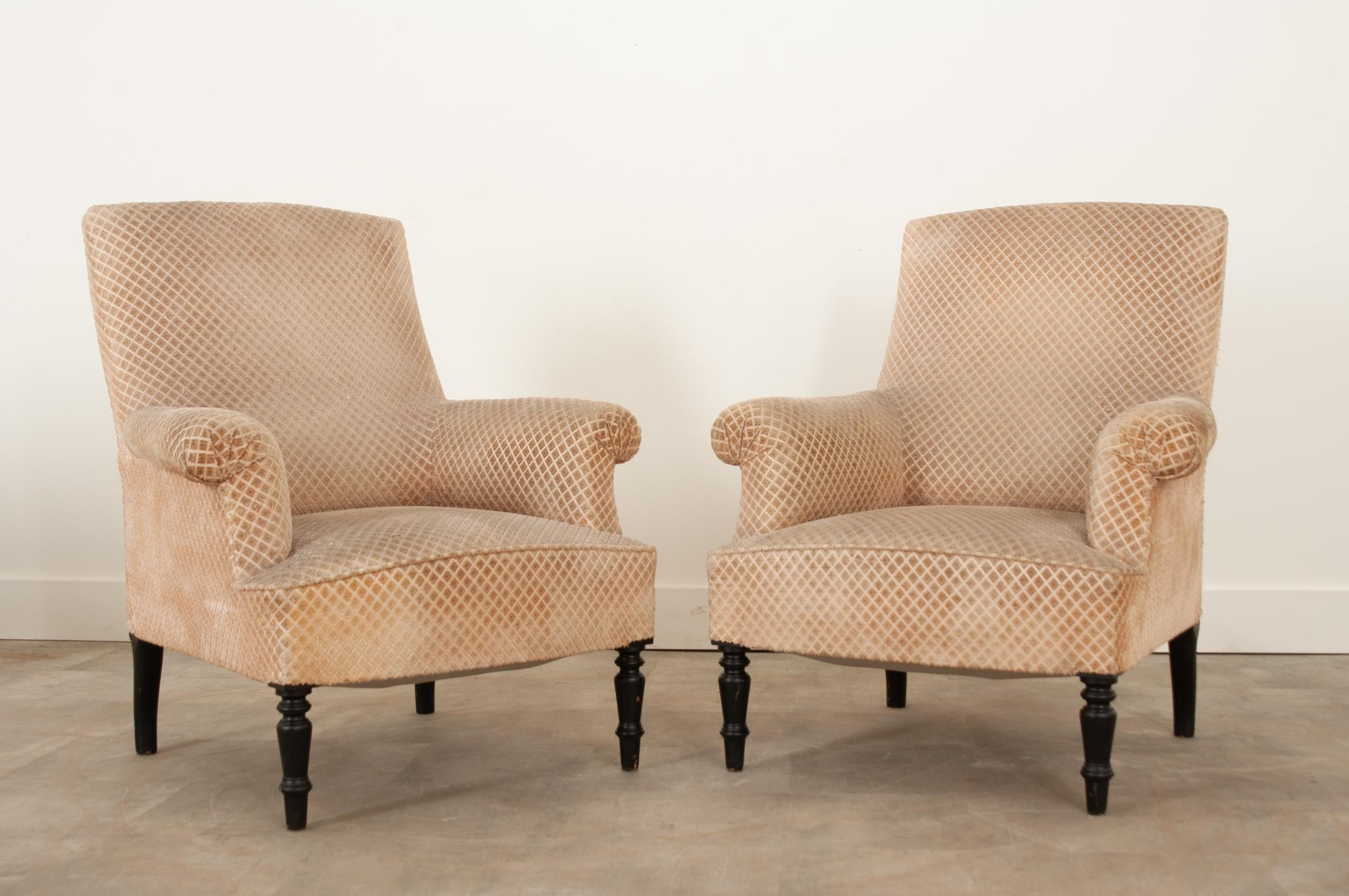 A classic pair of armchairs from 19th century England in wonderful antique condition. Upholstered in a neutral, patterned cut velvet fabric. Comfortable and sturdy, the chairs are raised on turned ebonized legs in the front, more simple legs in the