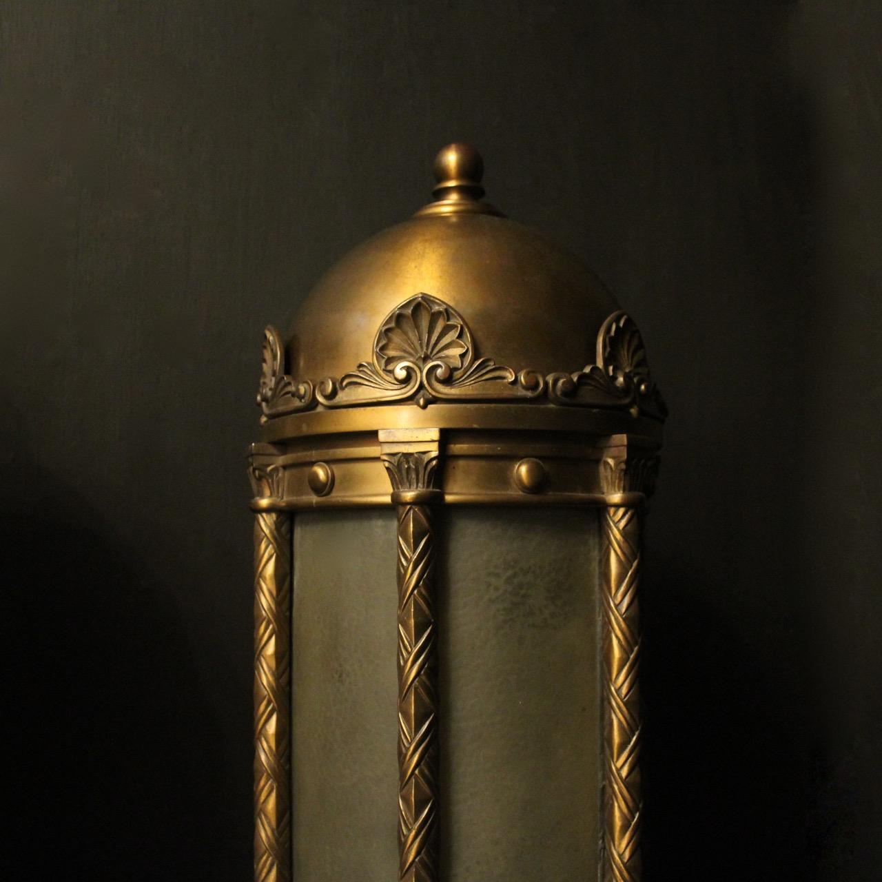 An English pair of single light bronze external antique wall lanterns, the original sectional frosted glass panels held within a lovely domed shaped ornate scrolling bronze framework with ribbon clad columns surrounded by a decorative Anthemion