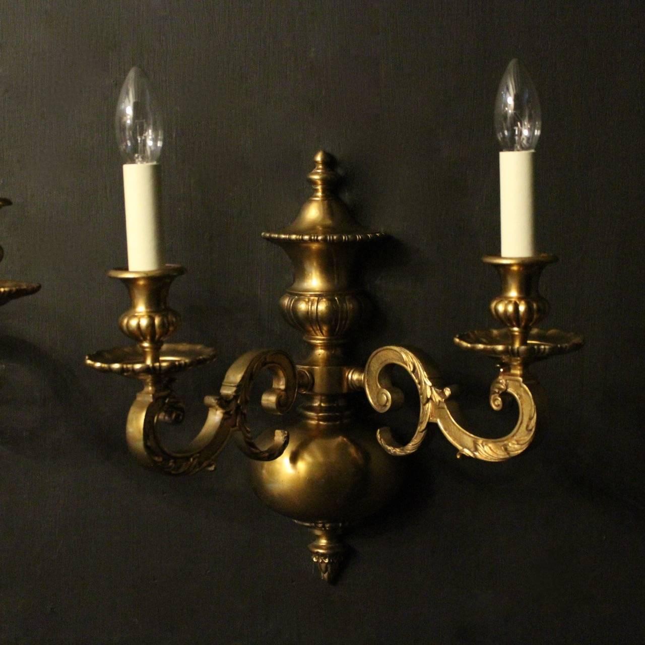 An English pair of gilded cast bronze twin arm antique wall lights, the square gauge leaf scrolling arms with circular sectional bobeches drip pans and reeded bulbous candle sconces, issuing from a decoratively cast elongated bulbous backplate, nice