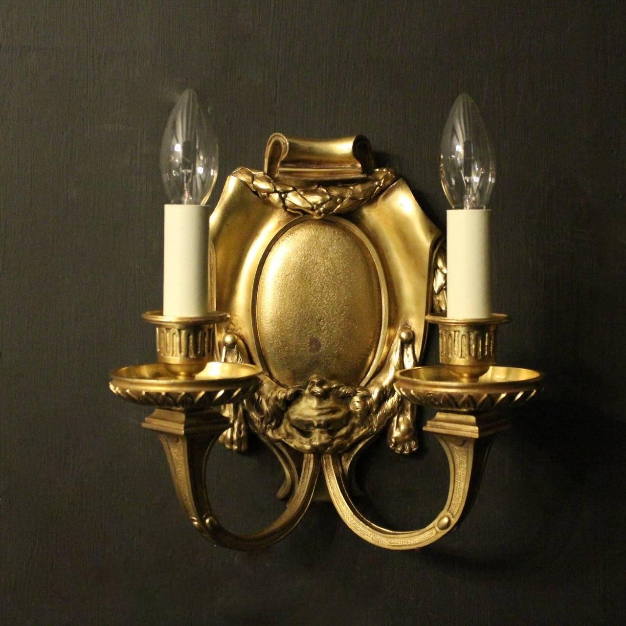 An English pair of gilded cast bronze twin arm antique wall lights, the tapering square gauge scrolling arms with circular leaf bobeche drip pans and reeded candle sconces, issuing from a decoratively cast cartouche shaped backplate with swaged