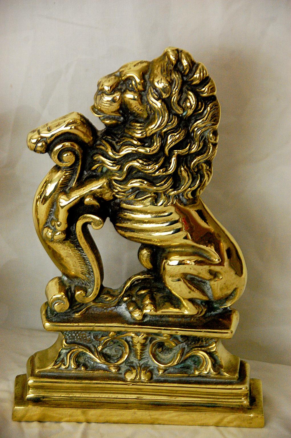 English pair of cast brass rampant lion doorstops of the 19th century. These heavy cast doorstops are a facing pair with bold molded detailing evident in the curly mane, whiskers and tongue, big paws and stepped base with leaf and swirl pattern.