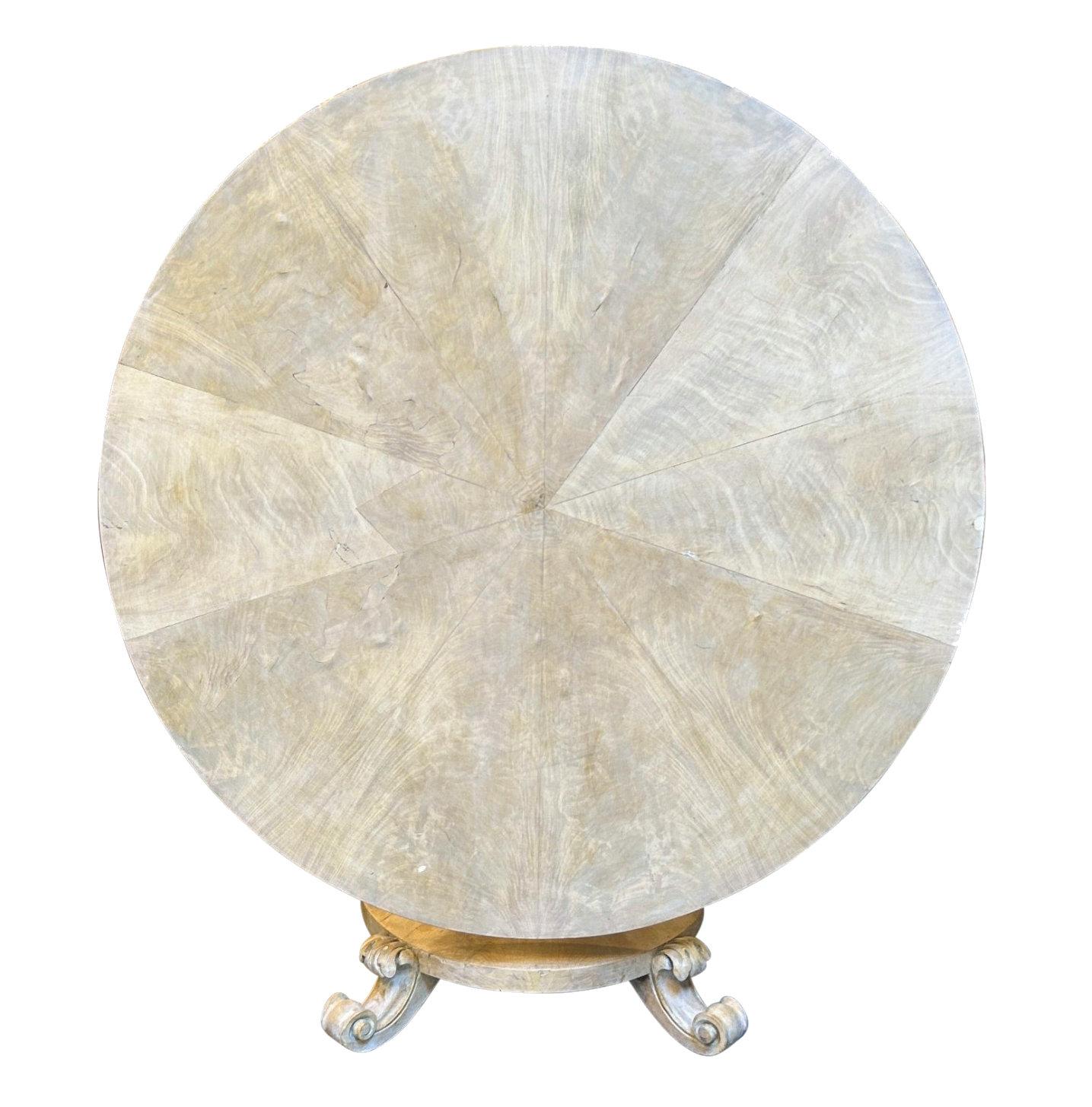 An English circular, tilt-top centre table in pickled mahogany. With a pedestal base on four acanthus feet and a sectional veneered top. The finish is one of aged parchment.