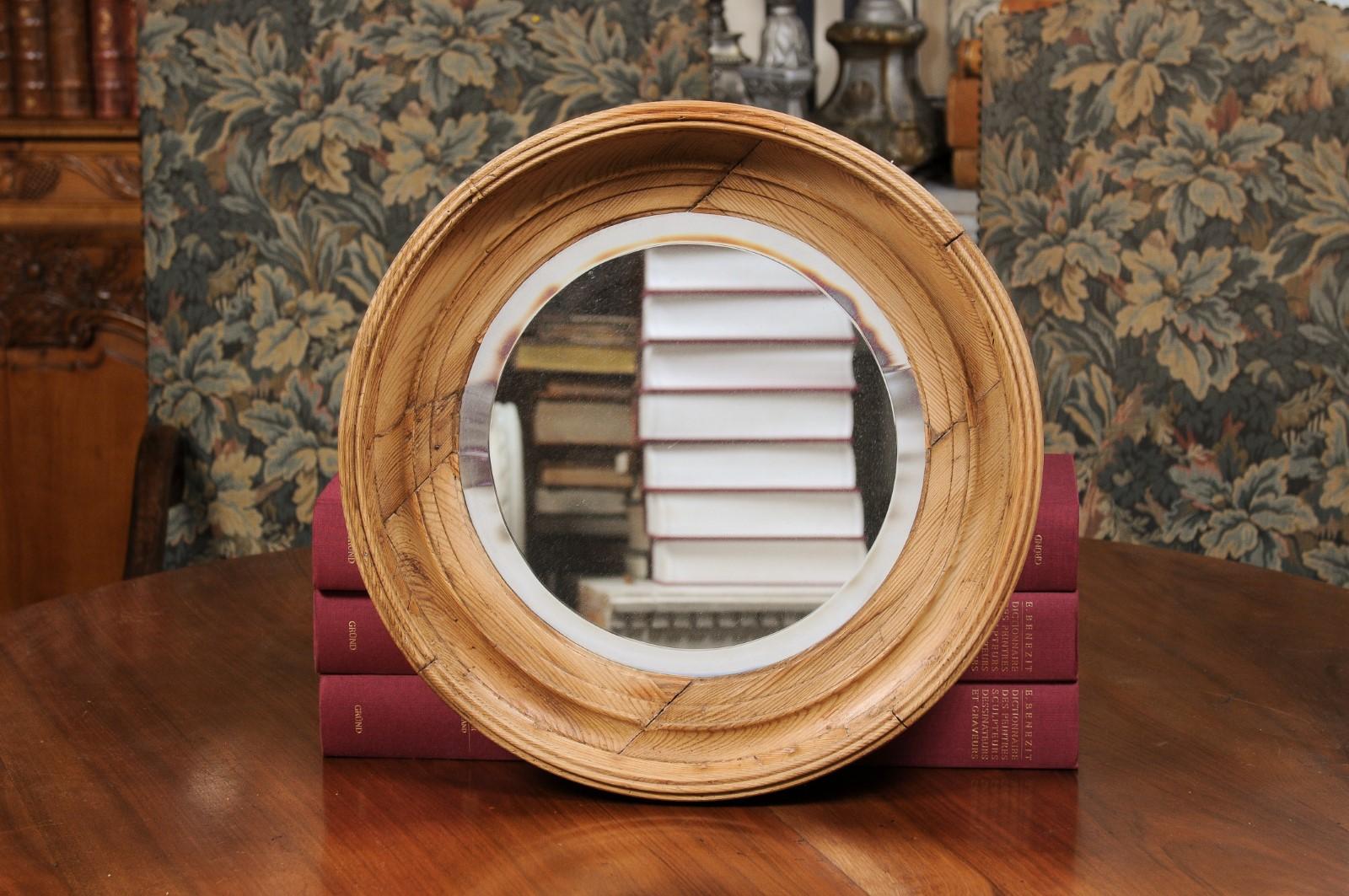 An English pine bullseye mirror from the 19th century, with natural patina and beveled glass. Created in England during the 19th century, this bullseye mirror features a pine molded circular frame surrounding a central mirror plate with beveled