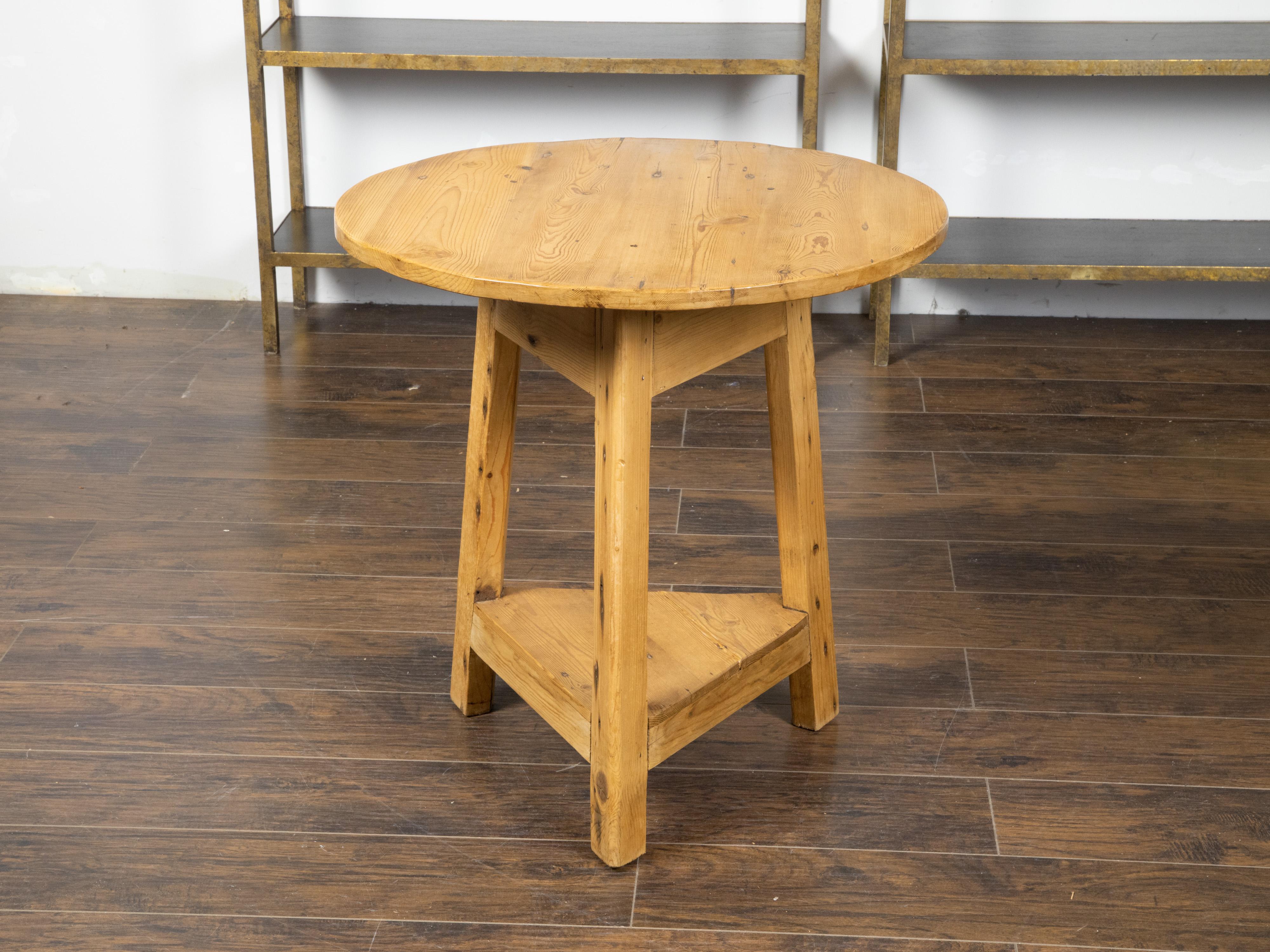 An English rustic pine cricket table from the 19th century, with circular top and triangular shelf. Created in England during the 19th century, this rustic cricket side table features a circular top, sitting above a simple triangular apron. The