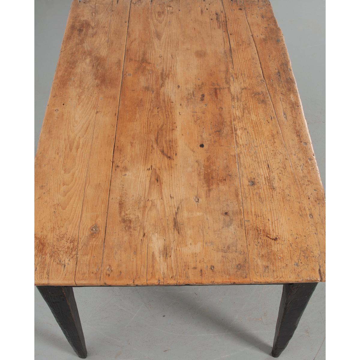 This English 19th century dining table or desk is made of pine. The top has been waxed over many years and has acquired a wonderful patina. The table base is painted a worn black finish and has a single offset drawer in the apron over tapered legs.
