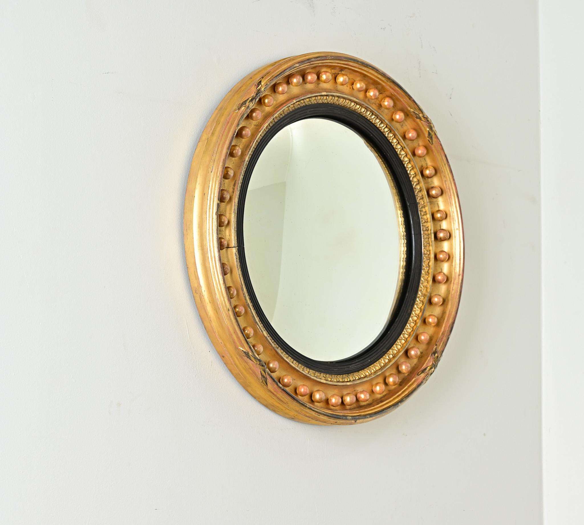 Ce miroir de style Régence anglaise serait tout à fait à sa place dans les styles de décoration d'intérieur d'aujourd'hui. Une plaque de miroir convexe est enchâssée dans une glissière ébénisée et cannelée, suivie de cercles concentriques d'autres