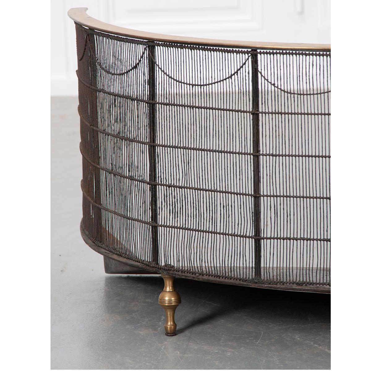 This is a beautiful English, brass and iron fire screen or nursery guard, circa 1830. It has a demilune shape with brass rail and feet. The iron framework and mesh-like surround has a swag design across the top just below the rail adding subtle