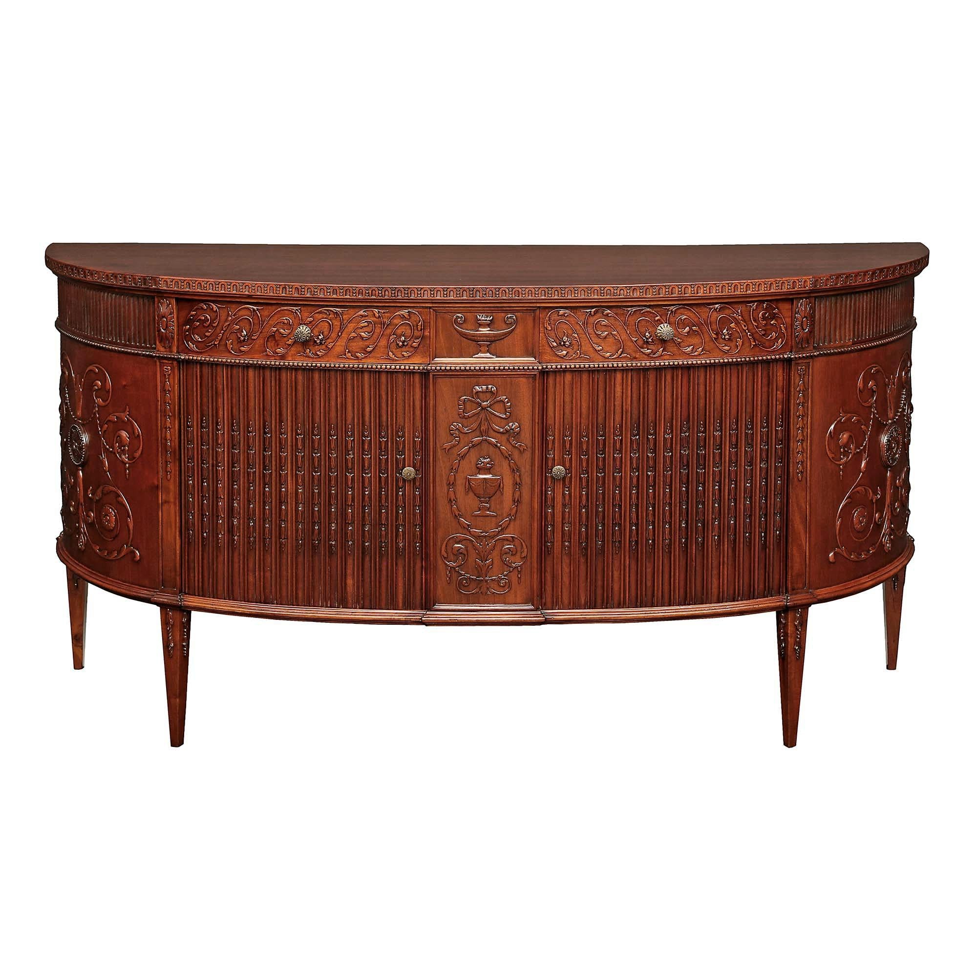 An outstanding English 19th century Regency mahogany two door, two drawer sideboard buffet. The buffet is raised by four square tapered legs with floral carvings. At the center is a finely carved urn on a recessed panel, framed within a tied ribbon