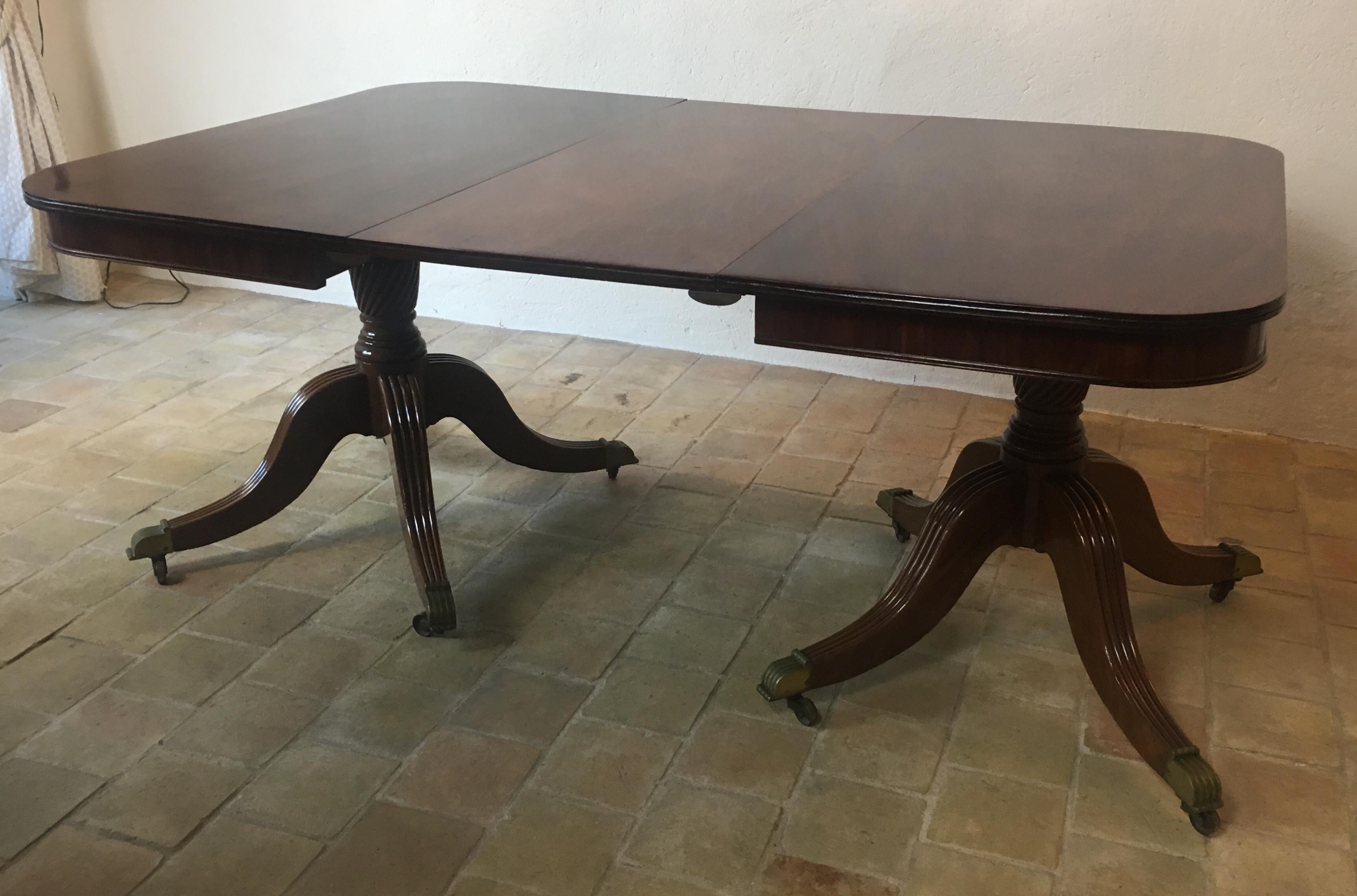 A superb quality English Regency dining table made of solid Cuban flame mahogany supported by two turned pillars/pedestals above four swept legs, terminating on brass casters. Extendable. 

The remarkable flame mahogany wood has a beautiful grain