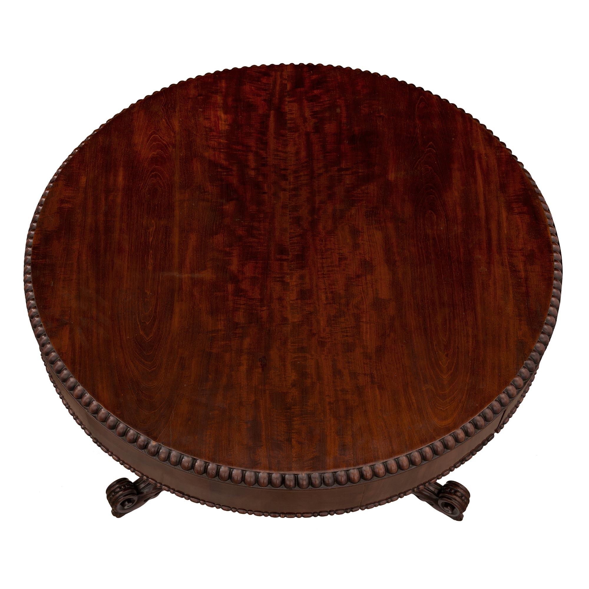 A most handsome English 19th century Regency st. flamed mahogany center table. The circular table is raised on its original carved wood casters below a beautiful finely carved tripod base. The base displays large acanthus leaves and an elegant