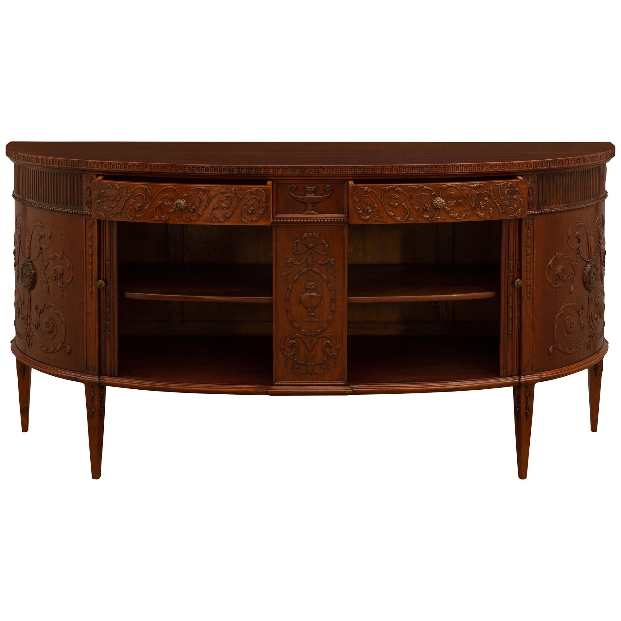 A wonderful and richly carved English 19th century Regency st. Mahogany buffet. The buffet is raised on four square tapered legs with floral top carvings. At the center is a finely carved urn on a recessed panel, framed within a tied ribbon and