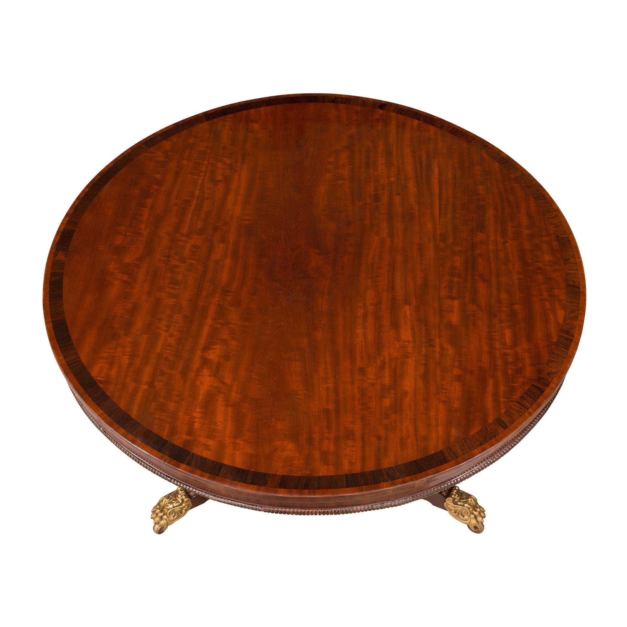 A handsome and extremely elegant English 19th century Regency st. mahogany, kingwood and ormolu center table. The table is raised by a triangular shaped base with concave sides and richly chased ormolu paw feet with their original casters. The