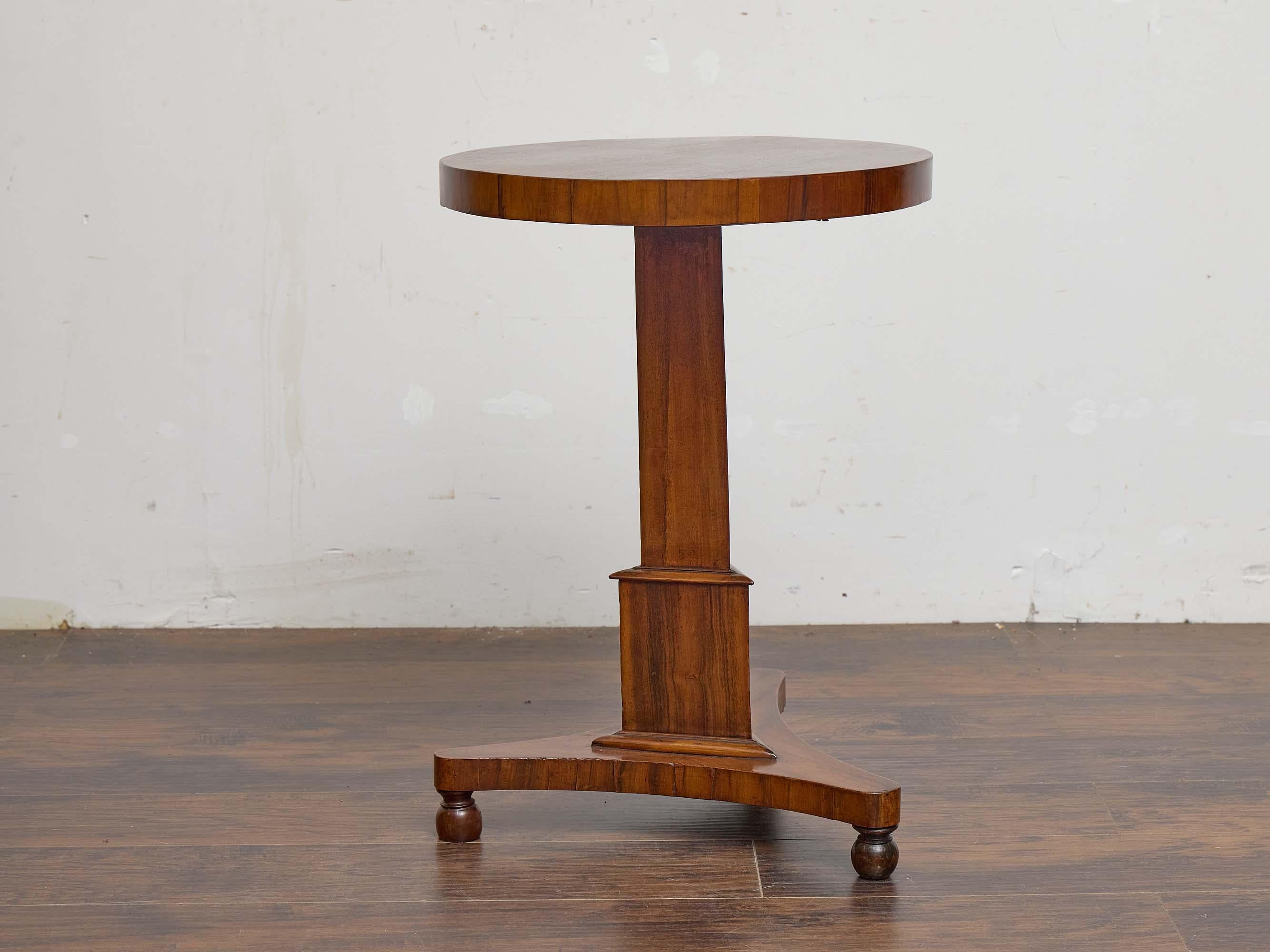 This English pedestal table from the 19th century is crafted in richly grained rosewood and features a balanced, architectural profile. The circular top rests on a faceted central column with molded detailing at the base, set atop a triangular