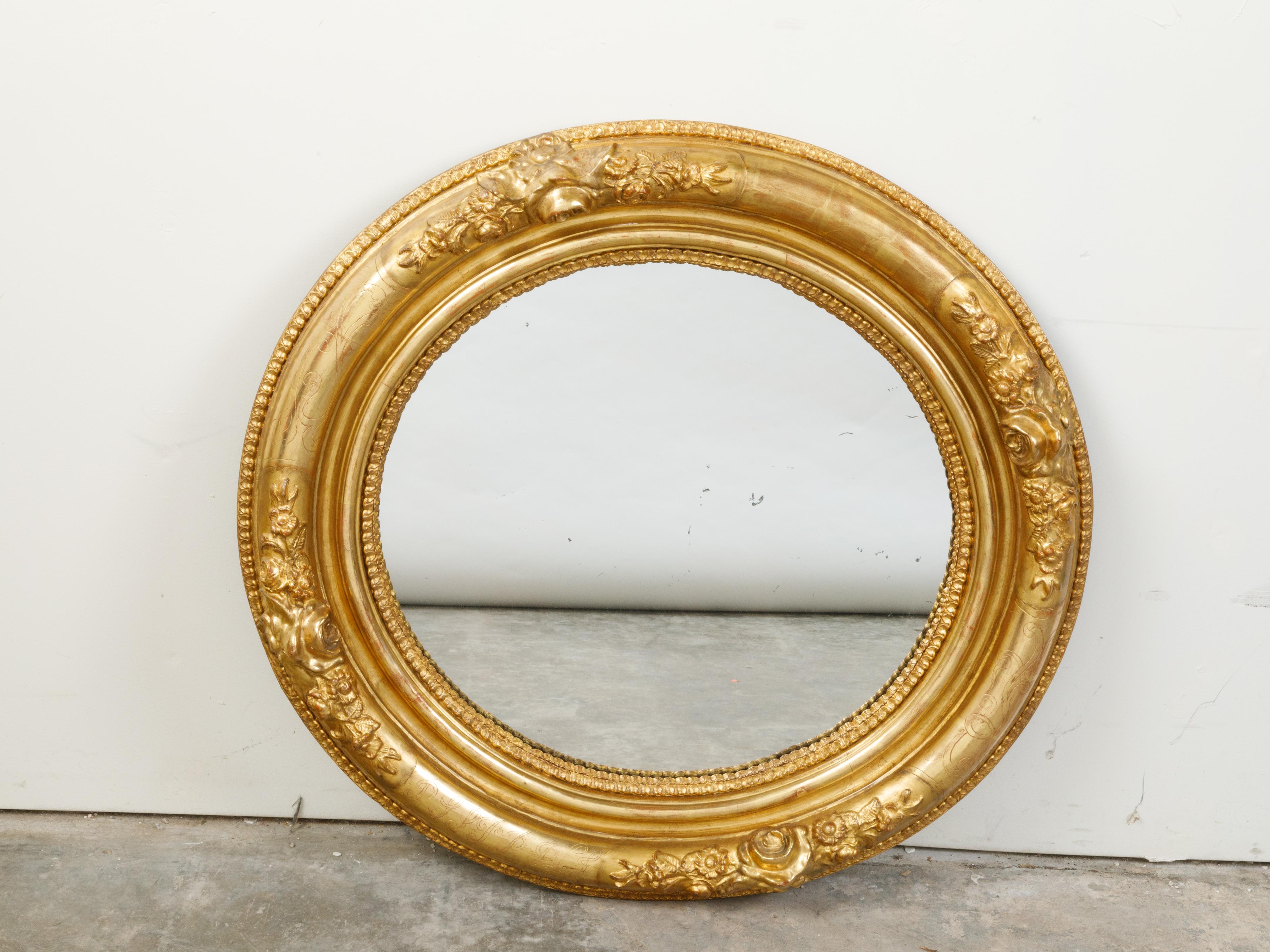 An English giltwood round mirror from the 19th century, with carved flowers and etched motifs. Created in England during the 19th century, this mirror features a circular giltwood frame adorned with carved flowers separated from one another through