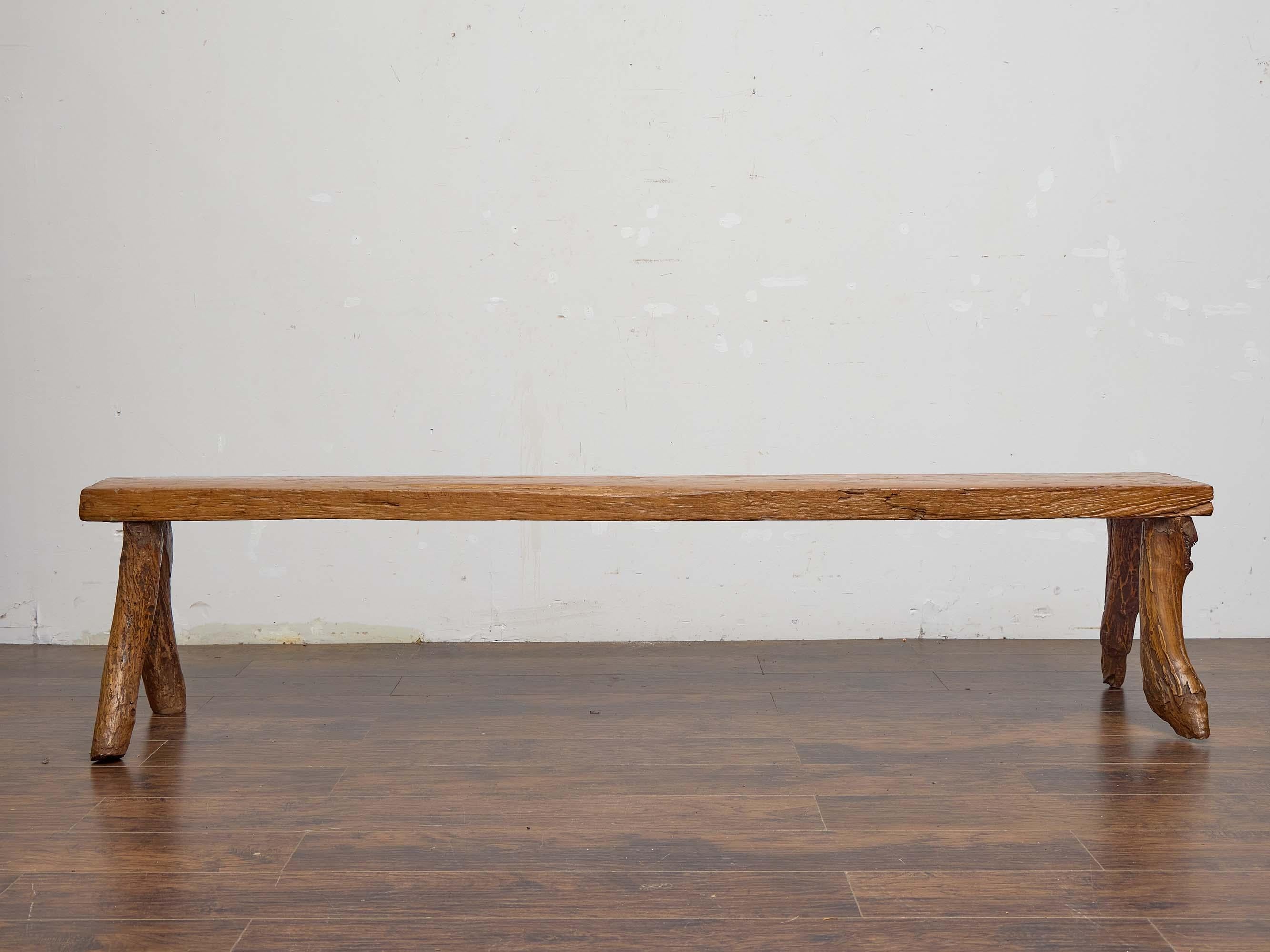 This 19th-century English bench captures the raw beauty and authenticity of rustic craftsmanship. Fashioned from solid elm, it features a thick, single-plank seat supported by boldly organic branch-form legs, each retaining the irregular shapes and