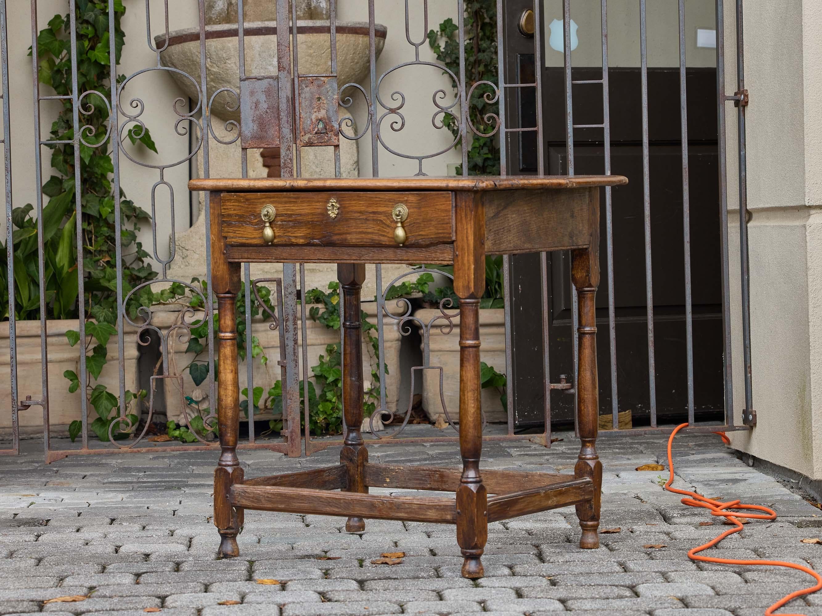 An English elm table from the 19th century, featuring a single drawer and turned supports. The rectangular top, with rounded edges, sits above a plain apron fitted with a central drawer, dressed with brass drop pulls and a decorative escutcheon