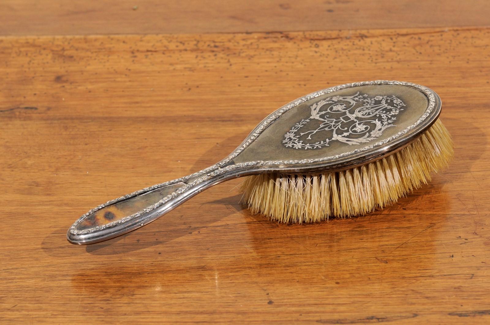 An English silver dressing table brush from the 19th century with silver piqué décor of lyre and floral arabesques. Born in England during the 19th century, this exquisite dressing table brush features an oval body, delicately adorned with a silver