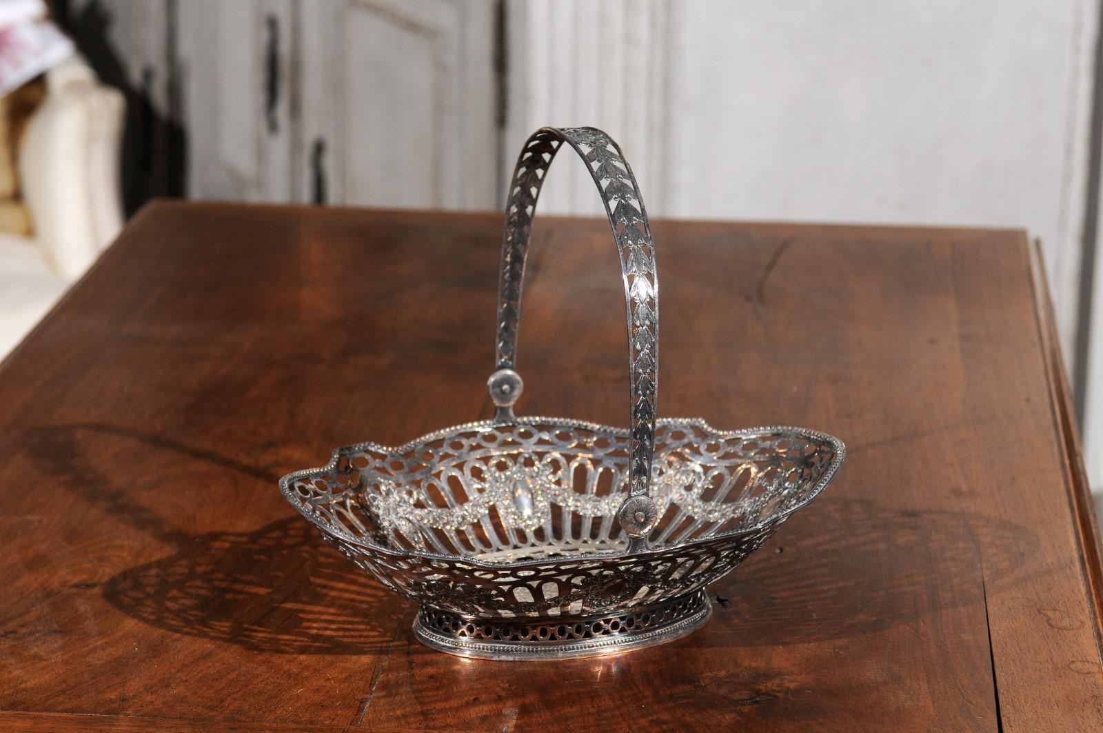An English silver plated bread basket from the 19th century, with intricate details and putti. Born in England during the 19th century, this exquisite silver plated bread basket features an oval pierced body, adorned with beads, garlands and putti