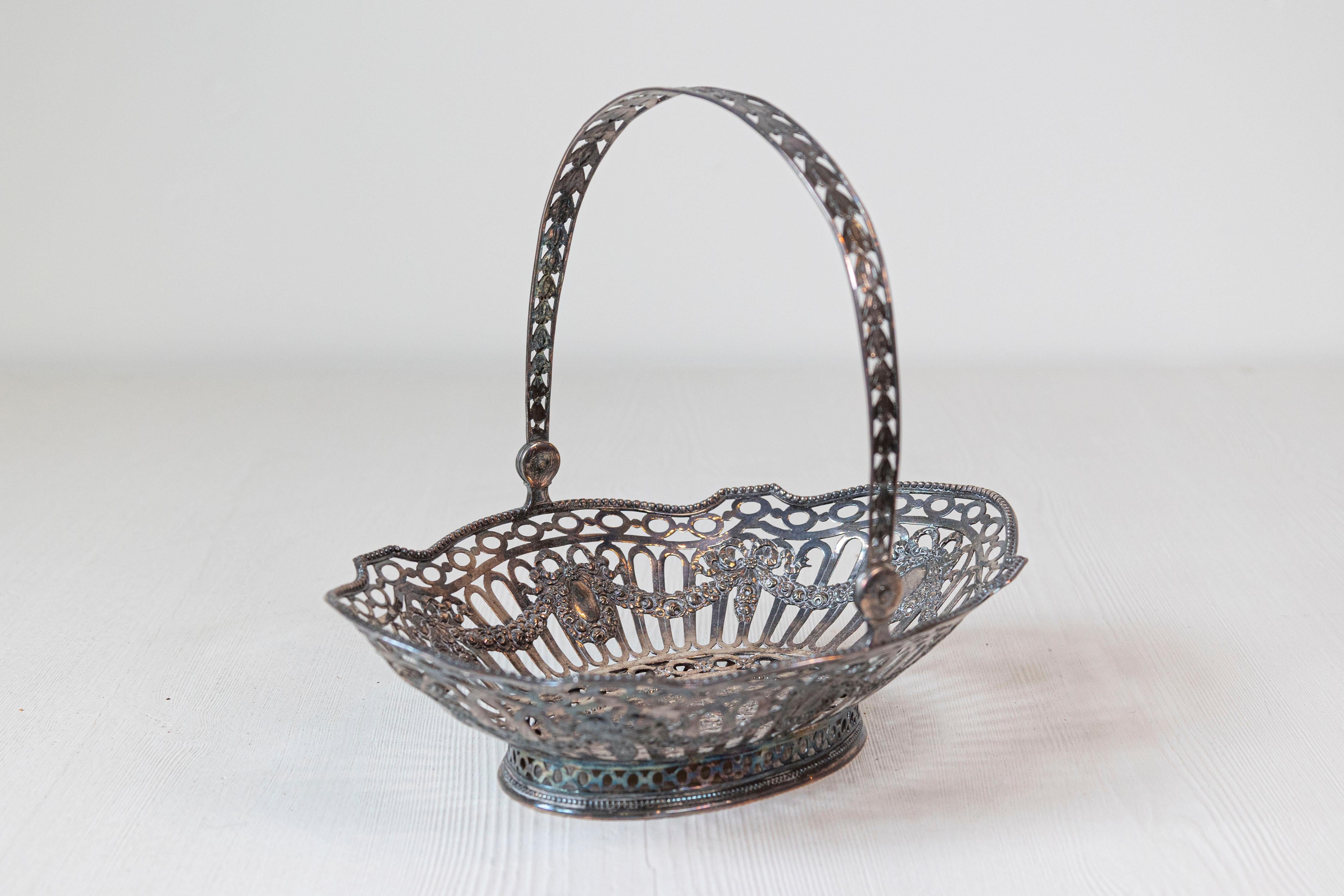 Panera inglesa bañada en plata del siglo XIX, con intrincados detalles y putti. Nacida en Inglaterra durante el siglo XIX, esta exquisita panera bañada en plata presenta un cuerpo oval perforado, adornado con cuentas, guirnaldas y putti en el