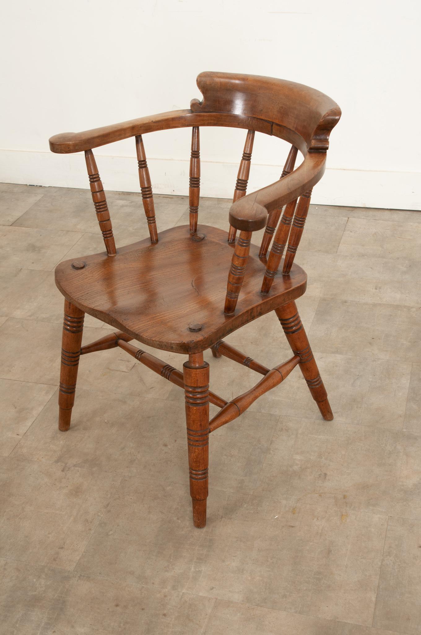 This late 19th century Victorian smokers bow arm chair dates from circa 1880 and is constructed of solid oak. It has a curved back with shaped arms, turned and hand-carved spindle upright supports and a figured shaped seat. This characterful antique