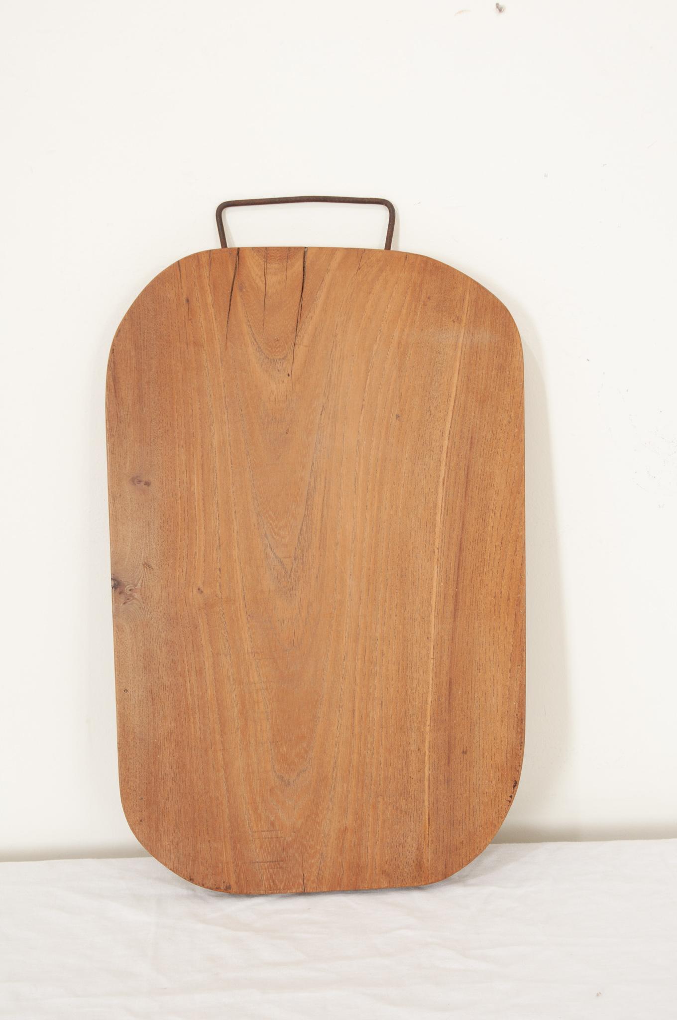 A 19th century long cutting board from England in an octagonal shape with smooth corners and a metal hanger on the end. The worn board is made of a single piece of wood. Knife marks and scrapes that were left by cooks, now long gone, can be seen and