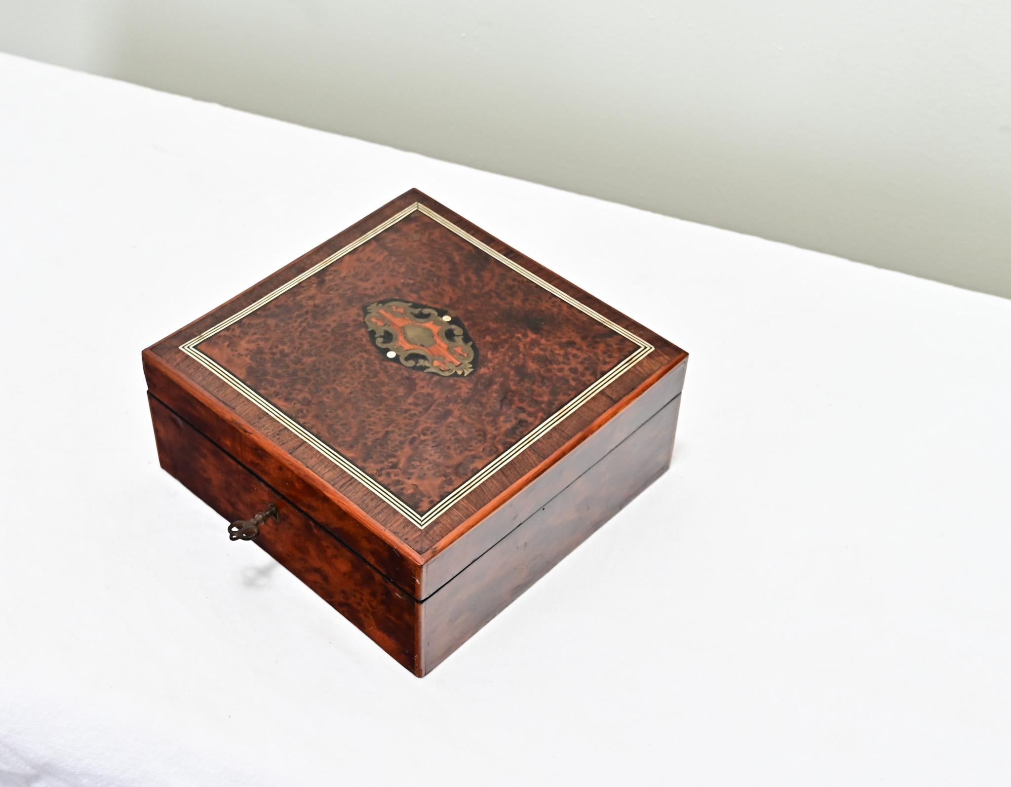 Un portagioie inglese in radica di mogano e intarsi del 1800. La parte superiore di questa scatola quadrata presenta un cartiglio intarsiato in ebano, acero e quercia con una fascia in ottone. La scatola si apre su cerniere in ottone e presenta un