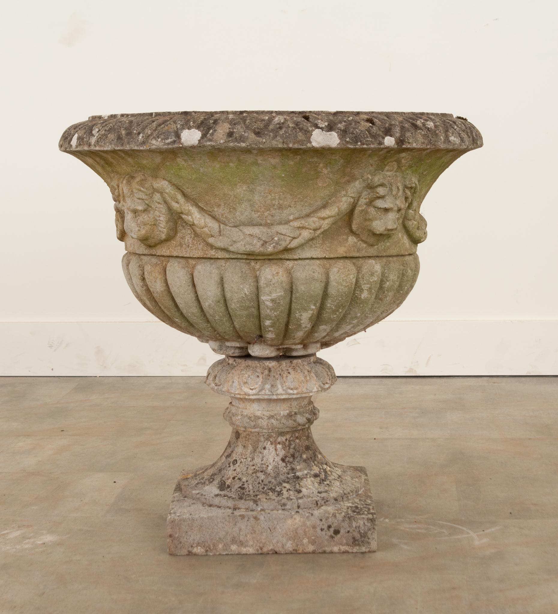 A stately stone pedestal planter from 19th century England. Ornamented with lion faces which connect with laurel swags. Holes for water drainage are present as well as a large screw for support. The top lifts from the base. It has gained a fantastic