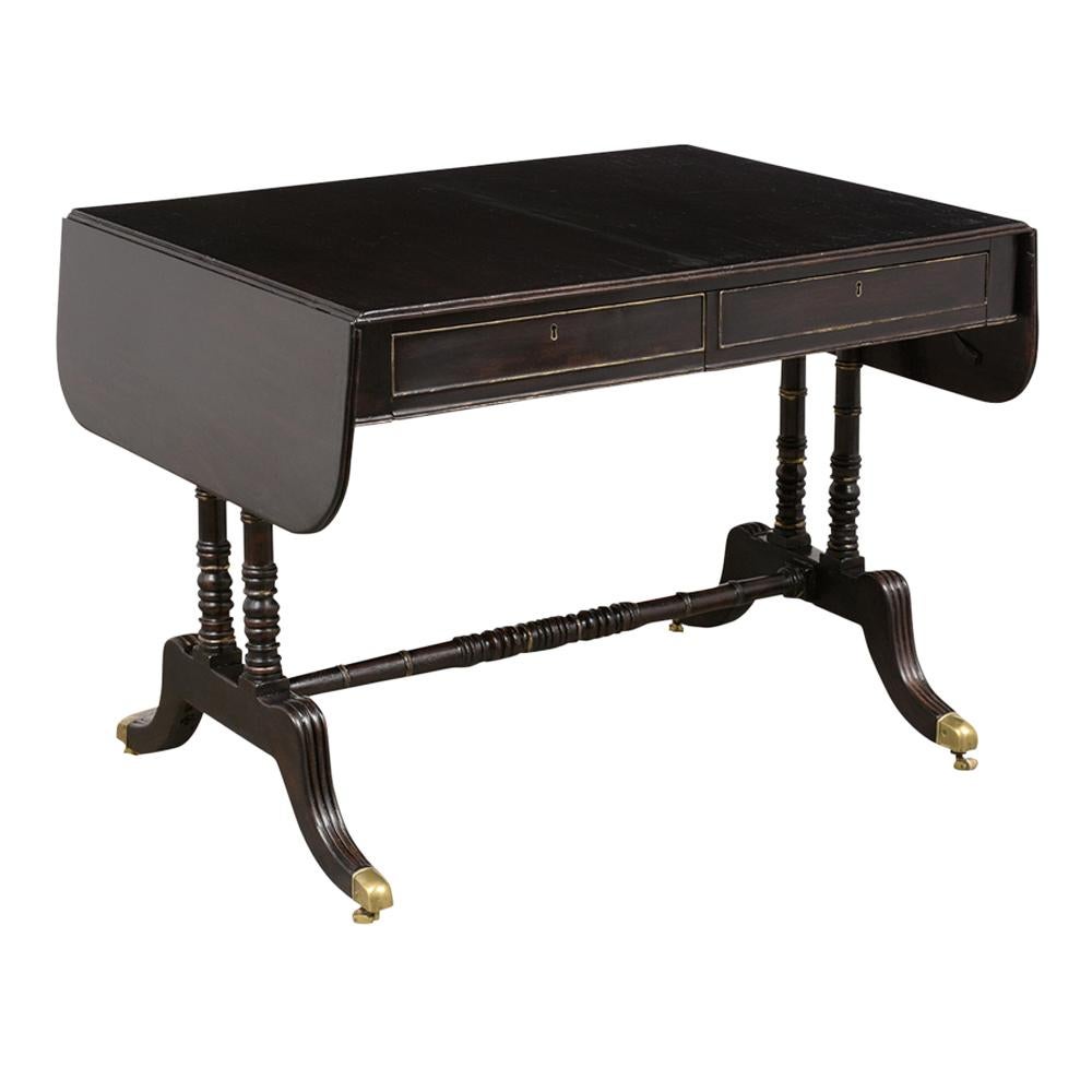 This Mid 19th Century English style Sofa Table is made out of mahogany wood with an ebonized patina finish and has been professionally restored. This writing table features two drop leaves, two front drawers that open with ease, and rests on sturdy