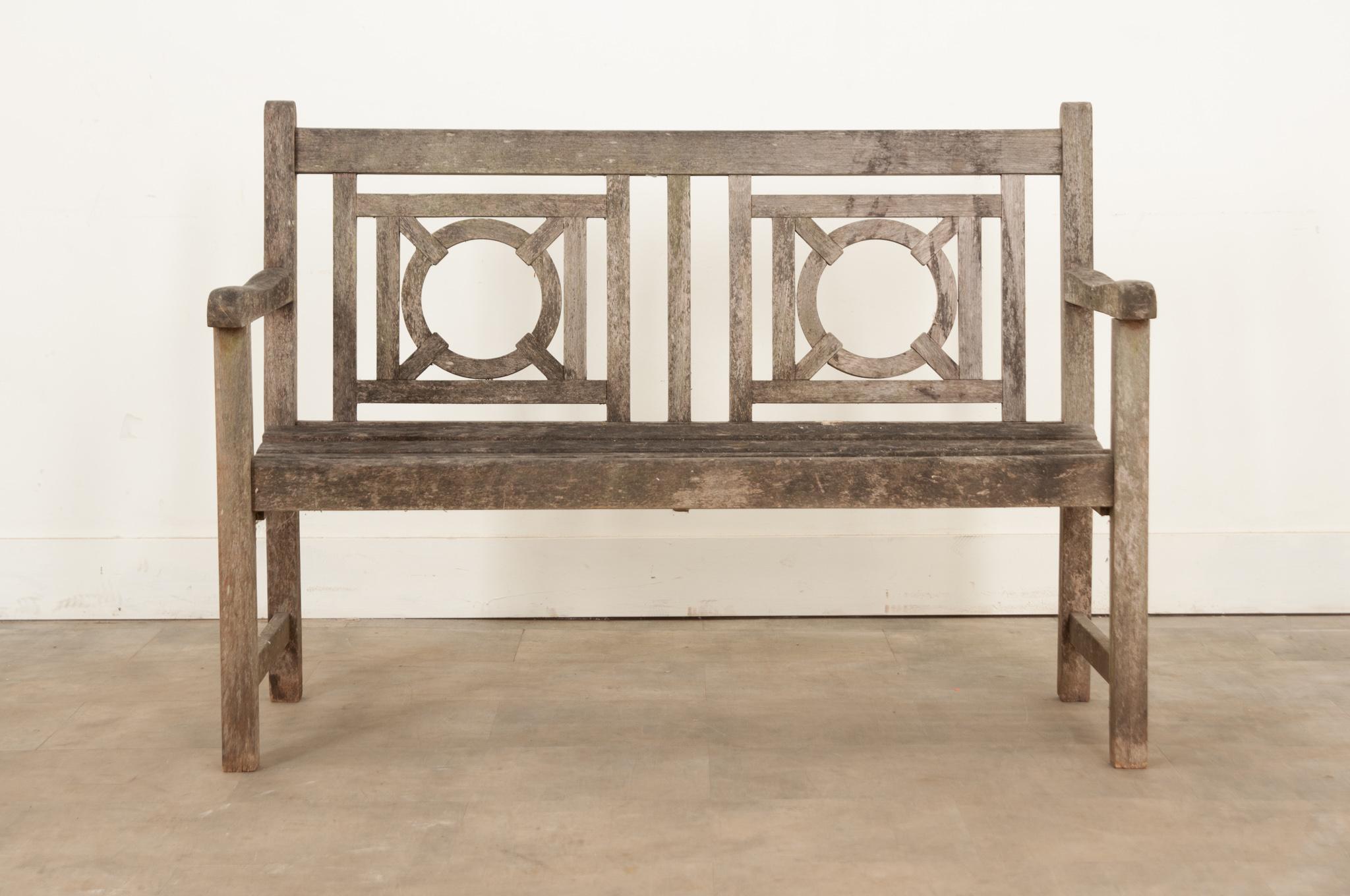 A fine English antique bench hand-crafted in the 19th century of teak wood. This attractive bench features a lovely weathered patina, a carved back, and a comfortable planked seat. The eye is drawn to its interesting geometric design that gives it a
