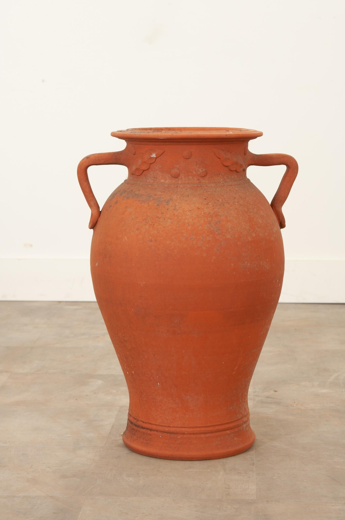 A beautiful unglazed terracotta urn from England, circa 1860. It has gained a great patina from years of exposure, giving it a unique texture and fleck of color. A pair of shaped handles attach within a freeze of stylized leaves and olives. Make