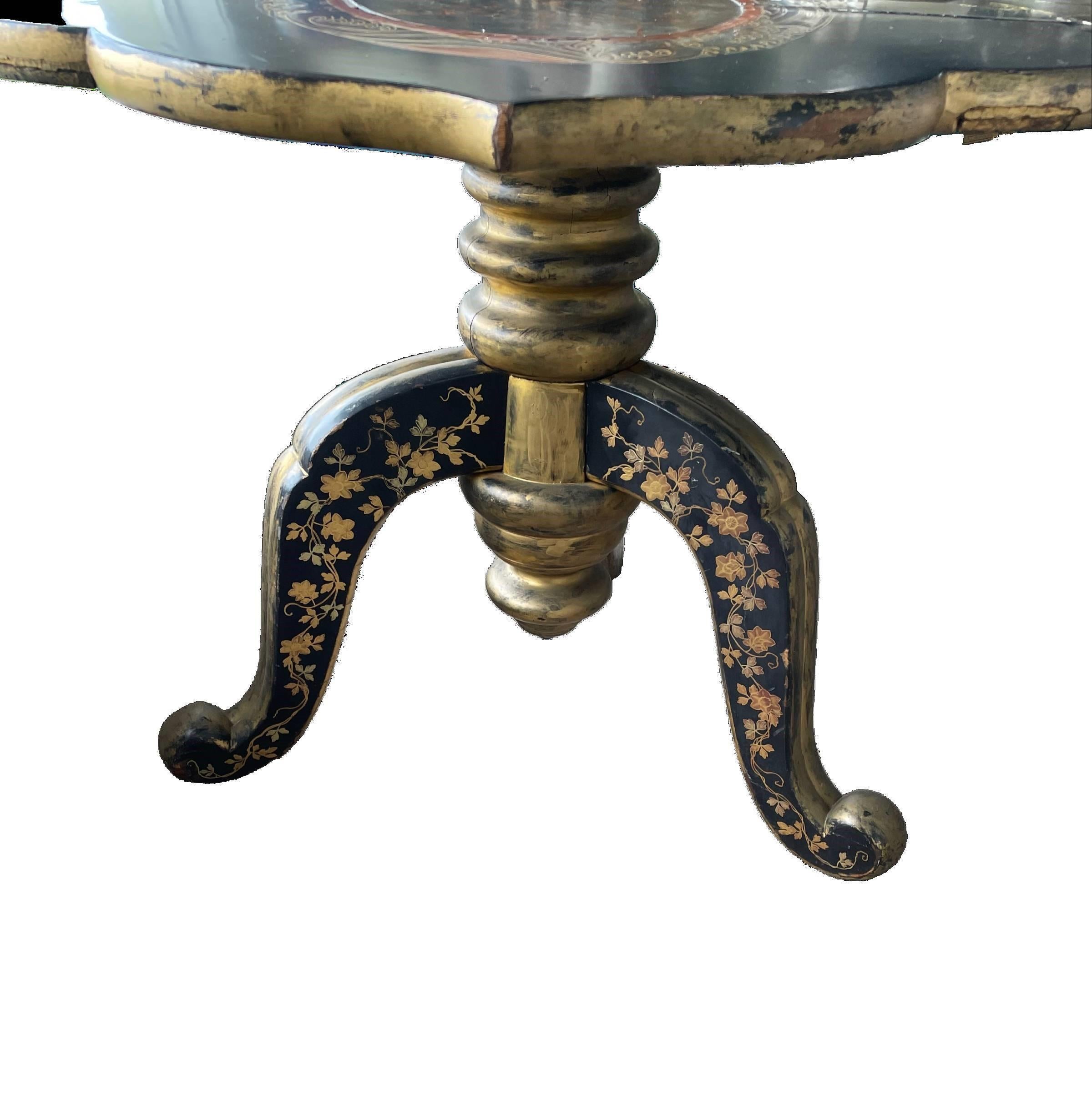 A Chinoiserie-themed antique wood table, finished in black lacquer has red and gold etching on the top and the legs. The solid, turned central stem is finished in gold. This elegant table folds down to a console piece.