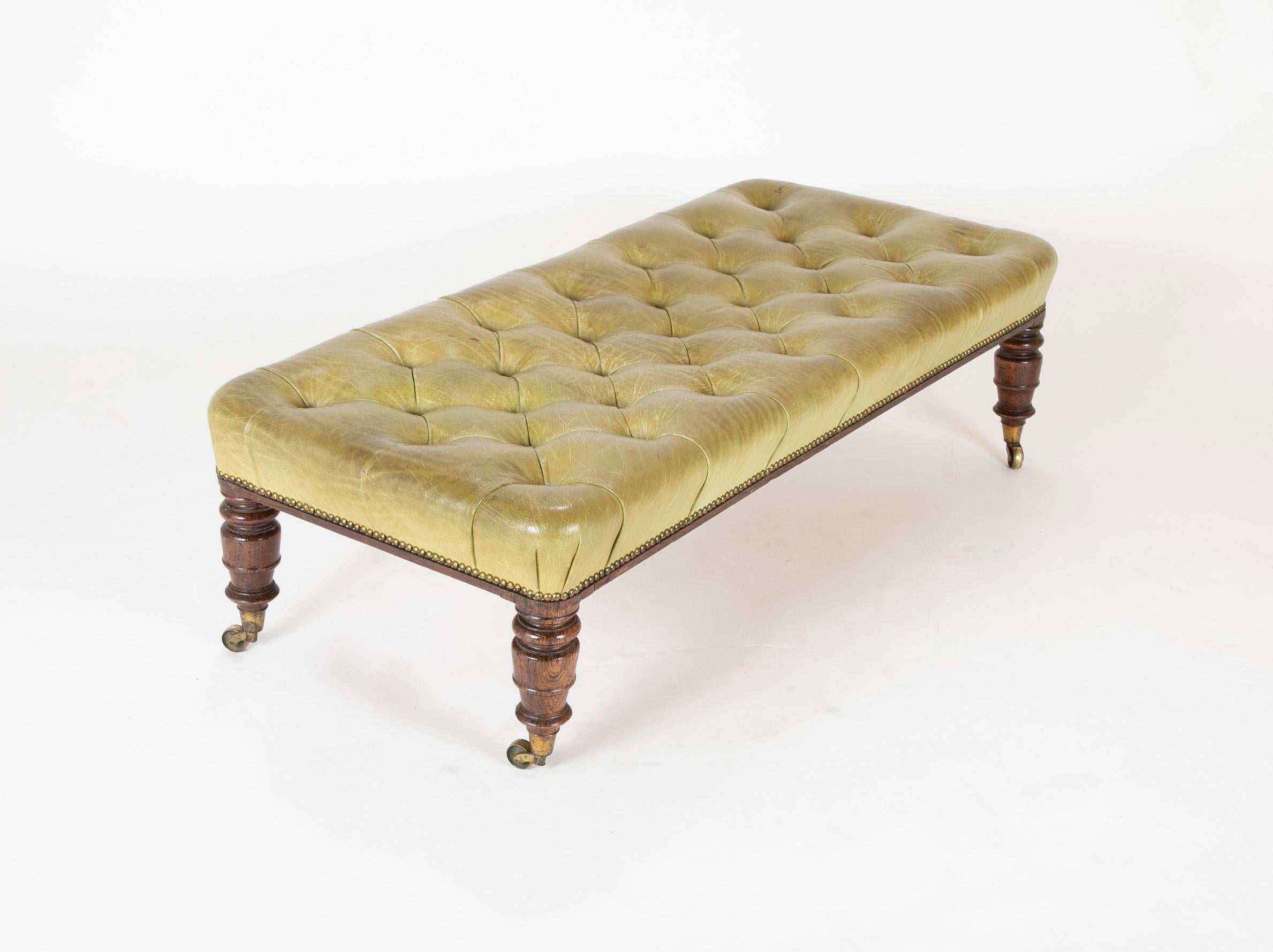 A 19th century English tufted green leather bench with brass nailed trim over tapering walnut turned legs ending on brass casters, circa 1880.