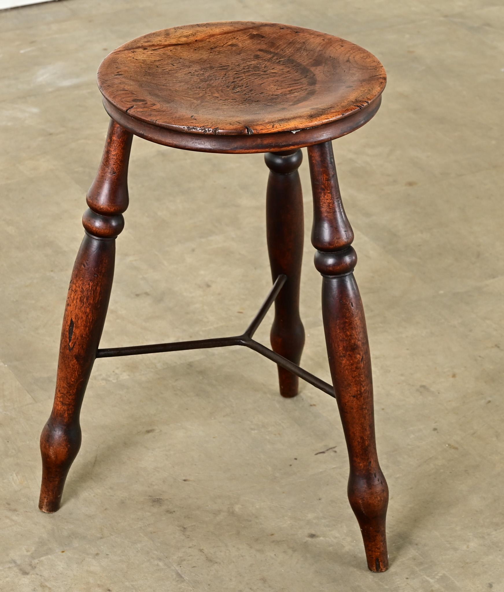Charmant tabouret en noyer provenant de l'Angleterre du XIXe siècle. Son design simple et pratique est rehaussé par des détails magnifiquement tournés qui embellissent les trois pieds et l'assise du tabouret. Les pieds sont reliés et renforcés par