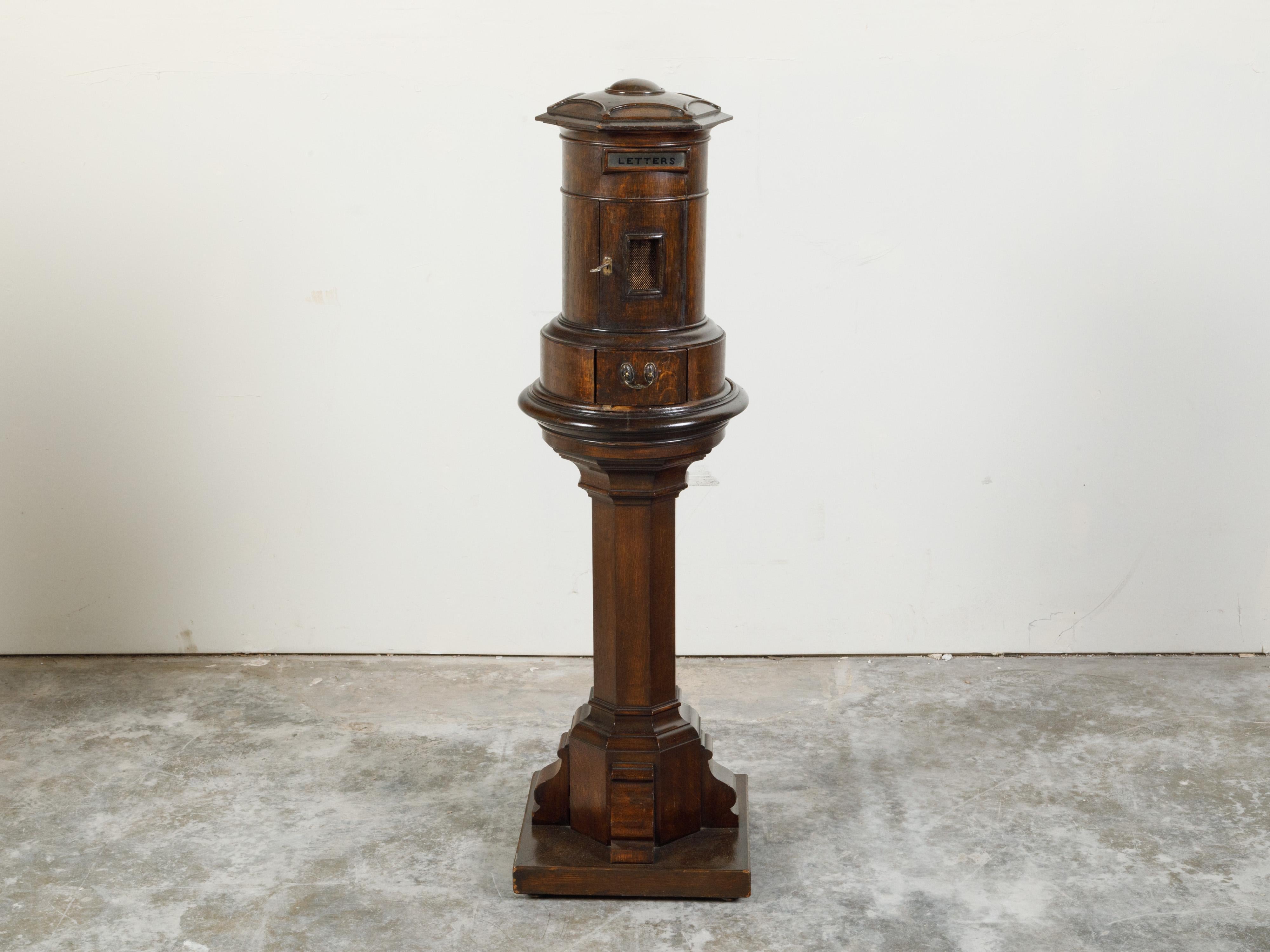 An English two-part wooden mailbox from the 19th century, with pedestal, petite door and drawer. Created in England during the 19th century, this wooden mailbox features a cylindrical top with petite door and drawer, sitting above an hexagonal