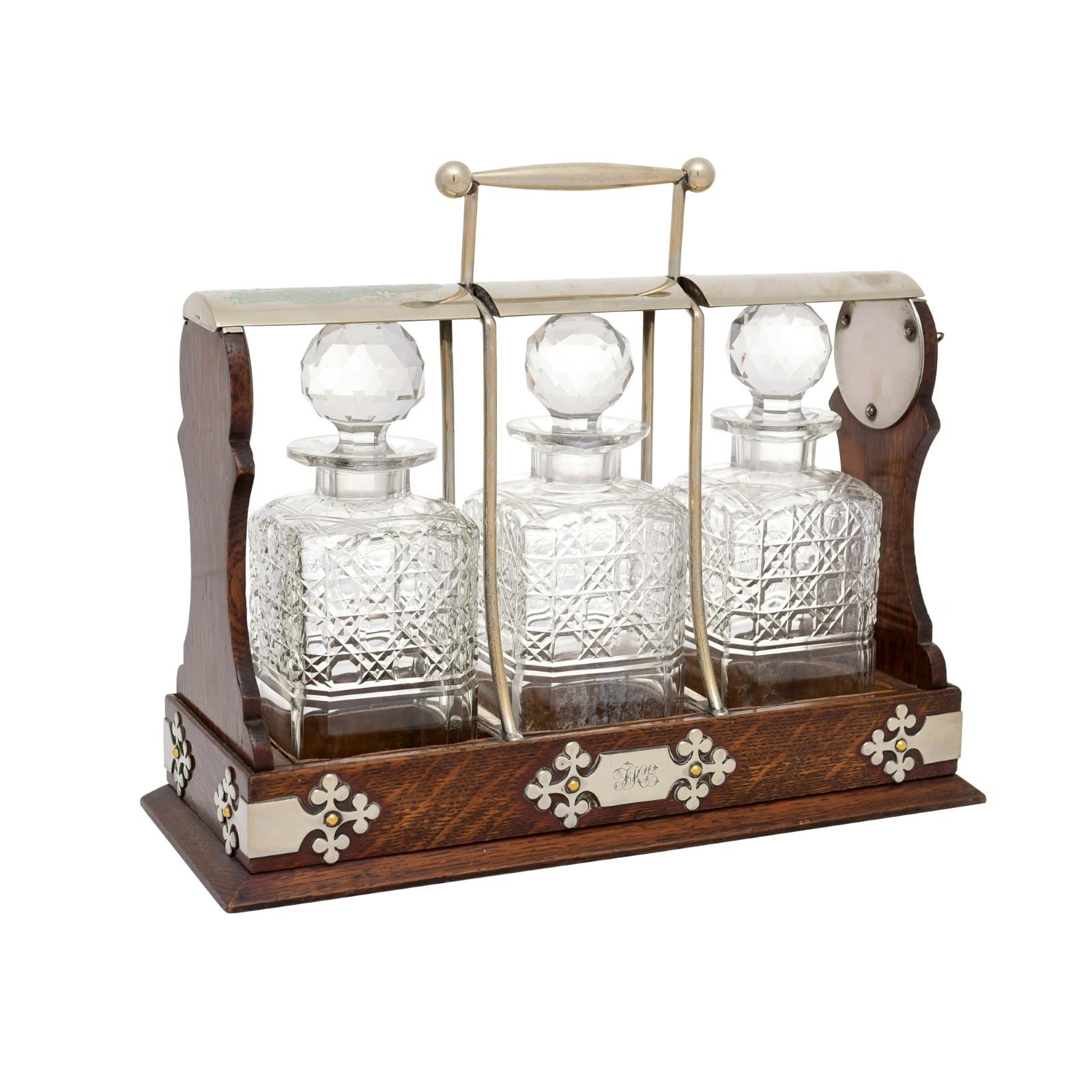 An English Victorian period wooden tantalus from the 19th century, with three cut glass decanters, key locking mechanism and silver metal accents. Created in England during the reign of Queen Victoria, this tantalus was designed to display the very