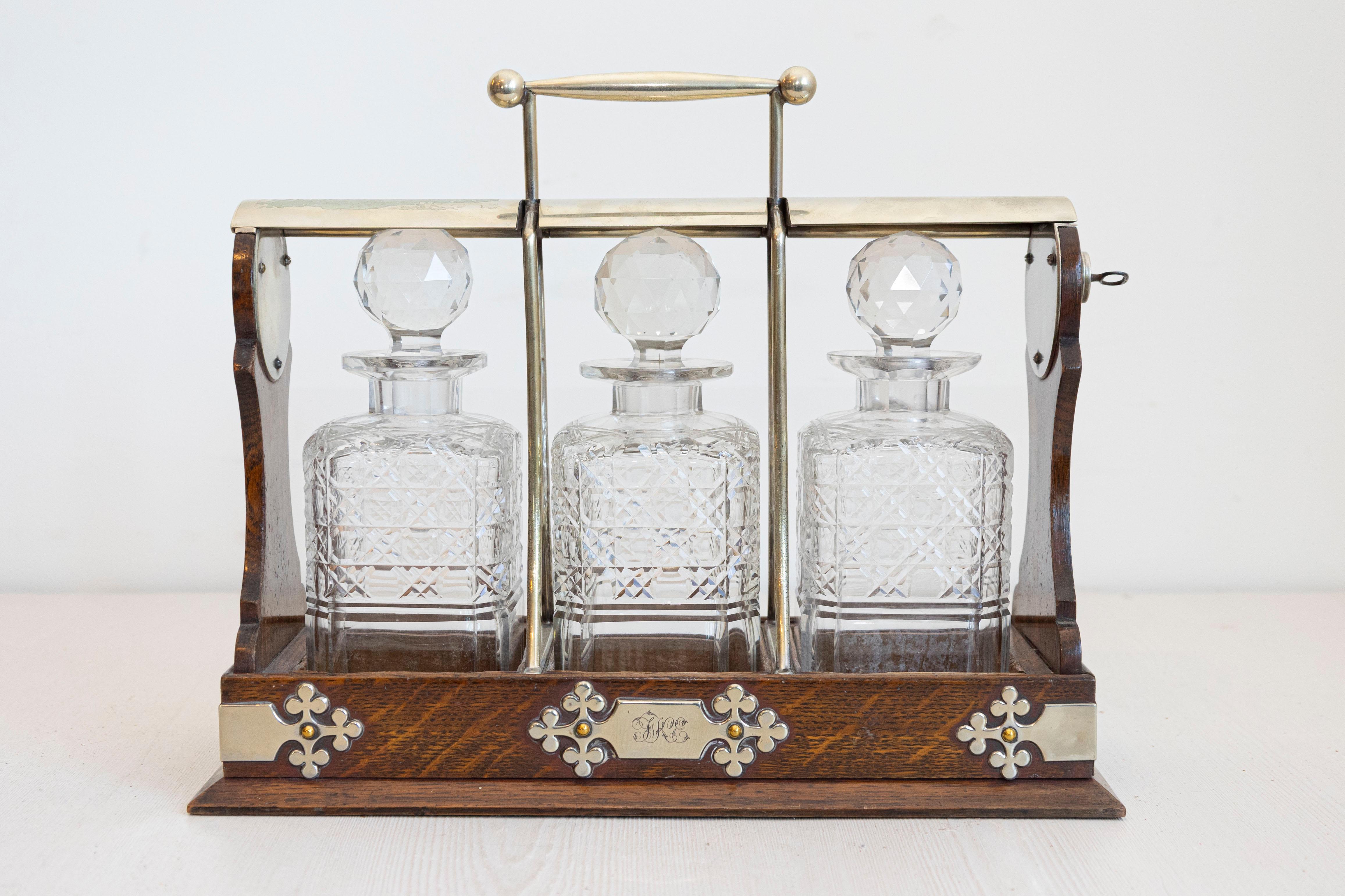 An English Victorian period wooden tantalus from the 19th century, with three cut glass decanters, key locking mechanism and silver metal accents. Created in England during the reign of Queen Victoria, this tantalus was designed to display the very