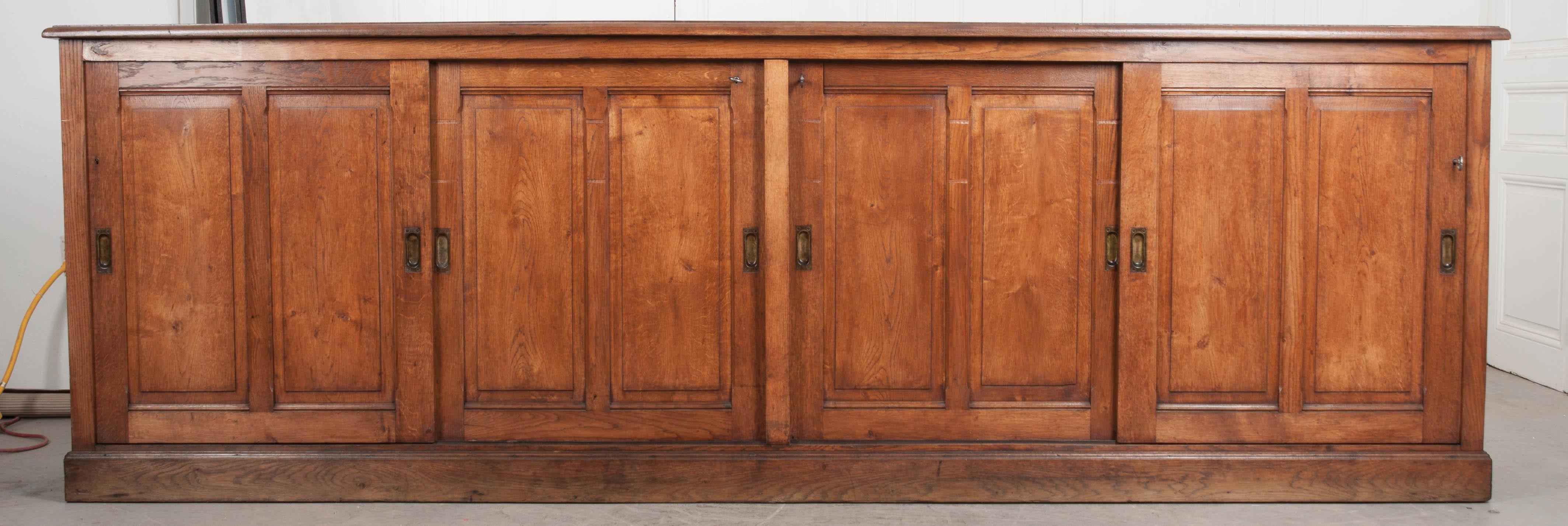 This large English Victorian oak sideboard, circa 1880s, with a rich burnt sienna finish, has four carved double-paneled sliding doors, with recessed pulls, which open to reveal two large storage spaces, each with a single fixed shelf, and