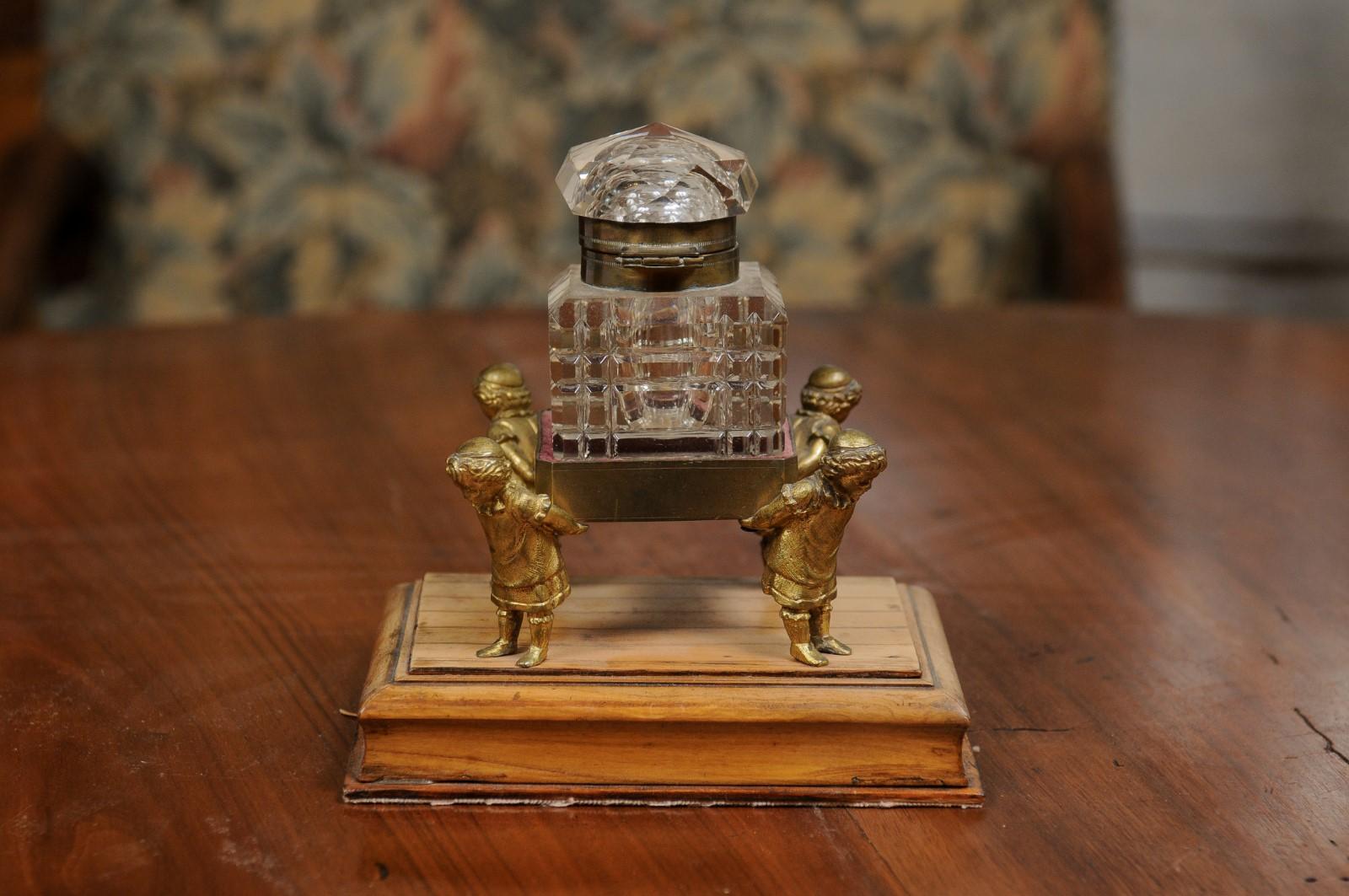 An English Victorian period crystal inkwell from the 19th century, with gilded children. Created in England during the 19th century, this inkwell captures our attention with its unusual depiction of four gilded children carrying a crystal inkwell