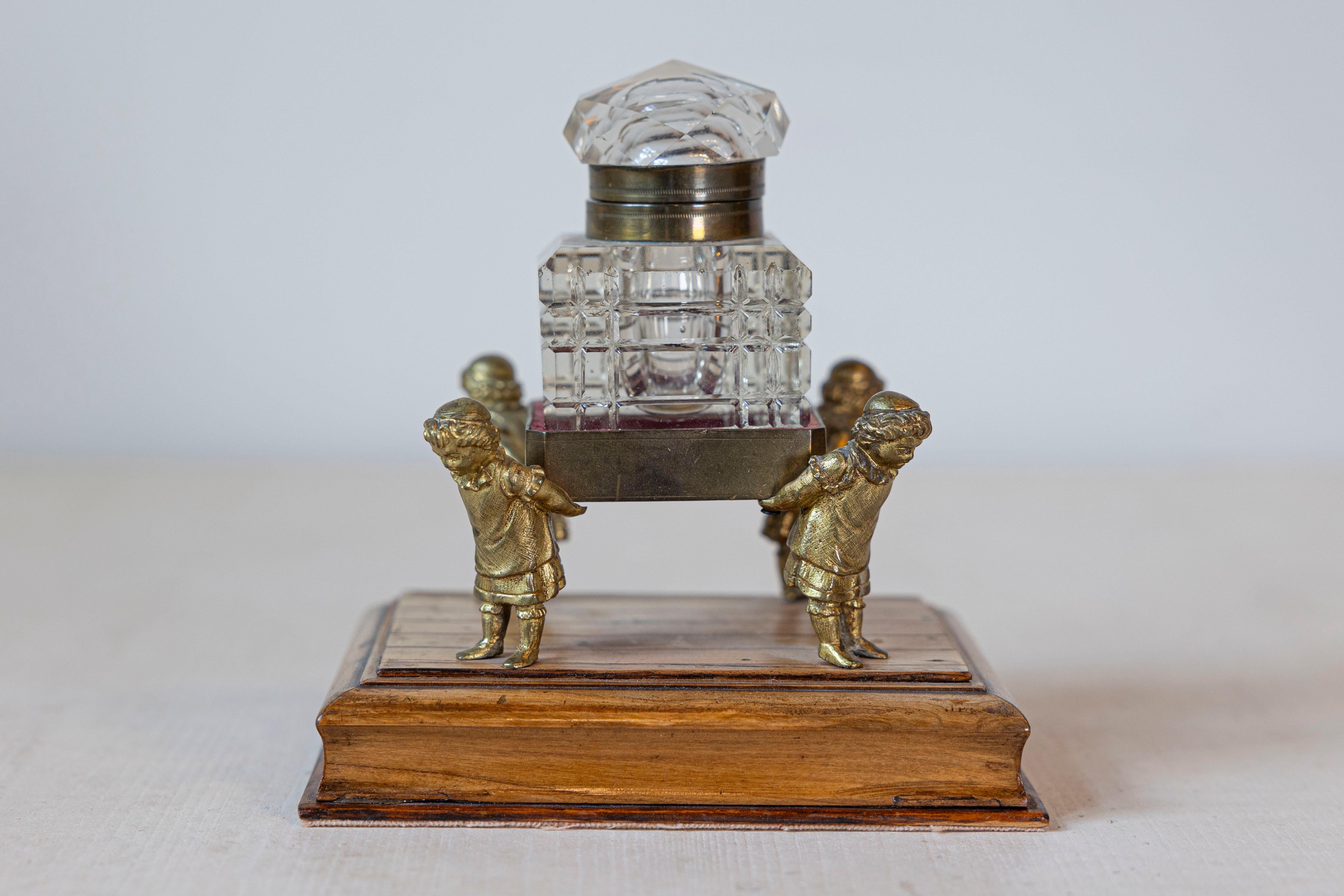 An English Victorian period crystal inkwell from the 19th century, with gilded children. Created in England during the 19th century, this inkwell captures our attention with its unusual depiction of four gilded children carrying a crystal inkwell